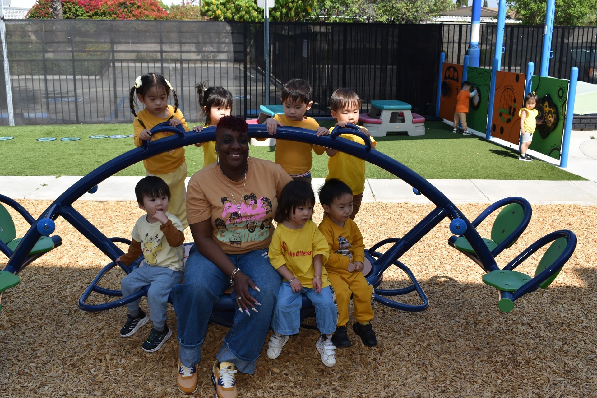 Woman and children in yellow shirts on playground, posing on a seesaw.
