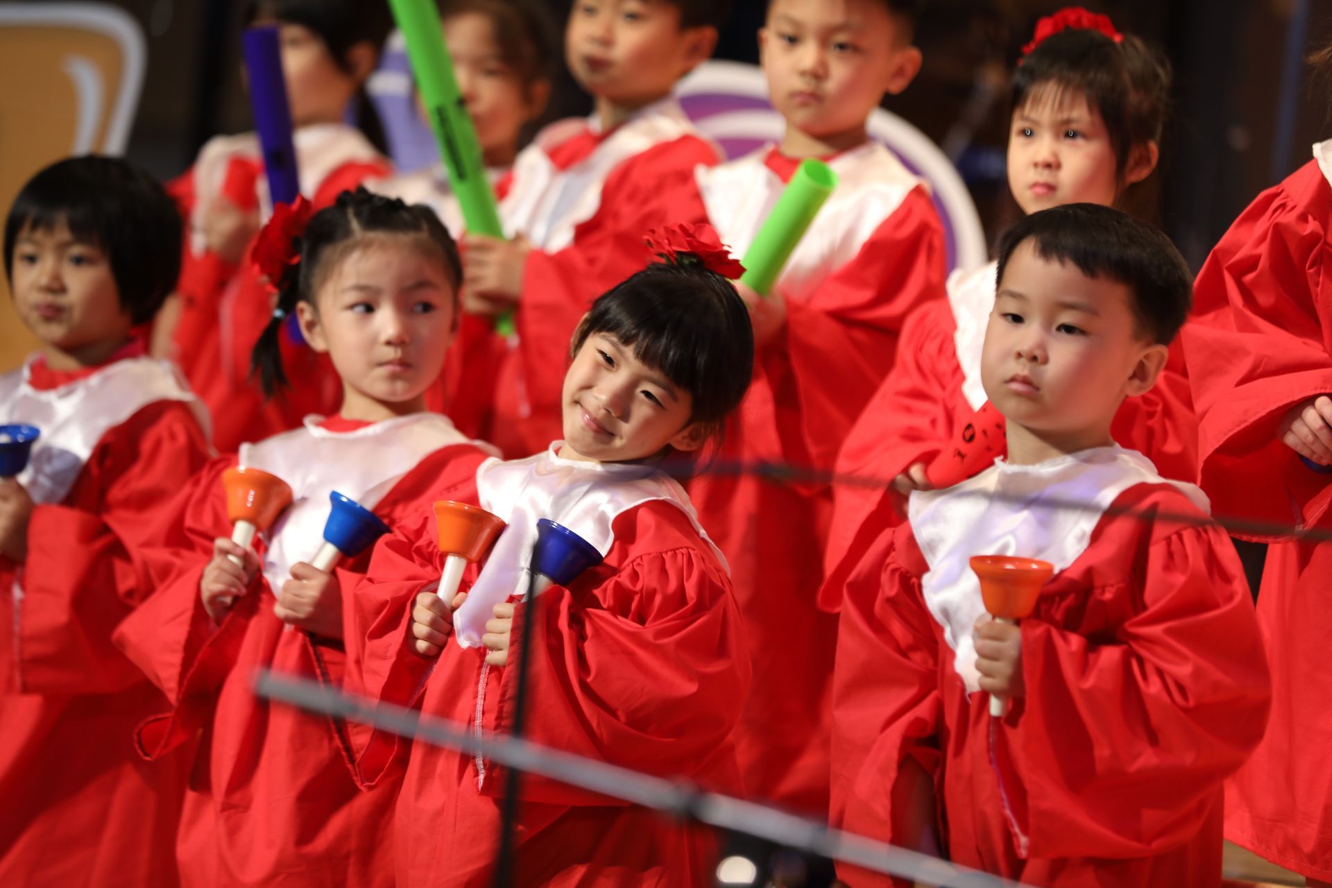 Children in red robes playing handbells on a stage.