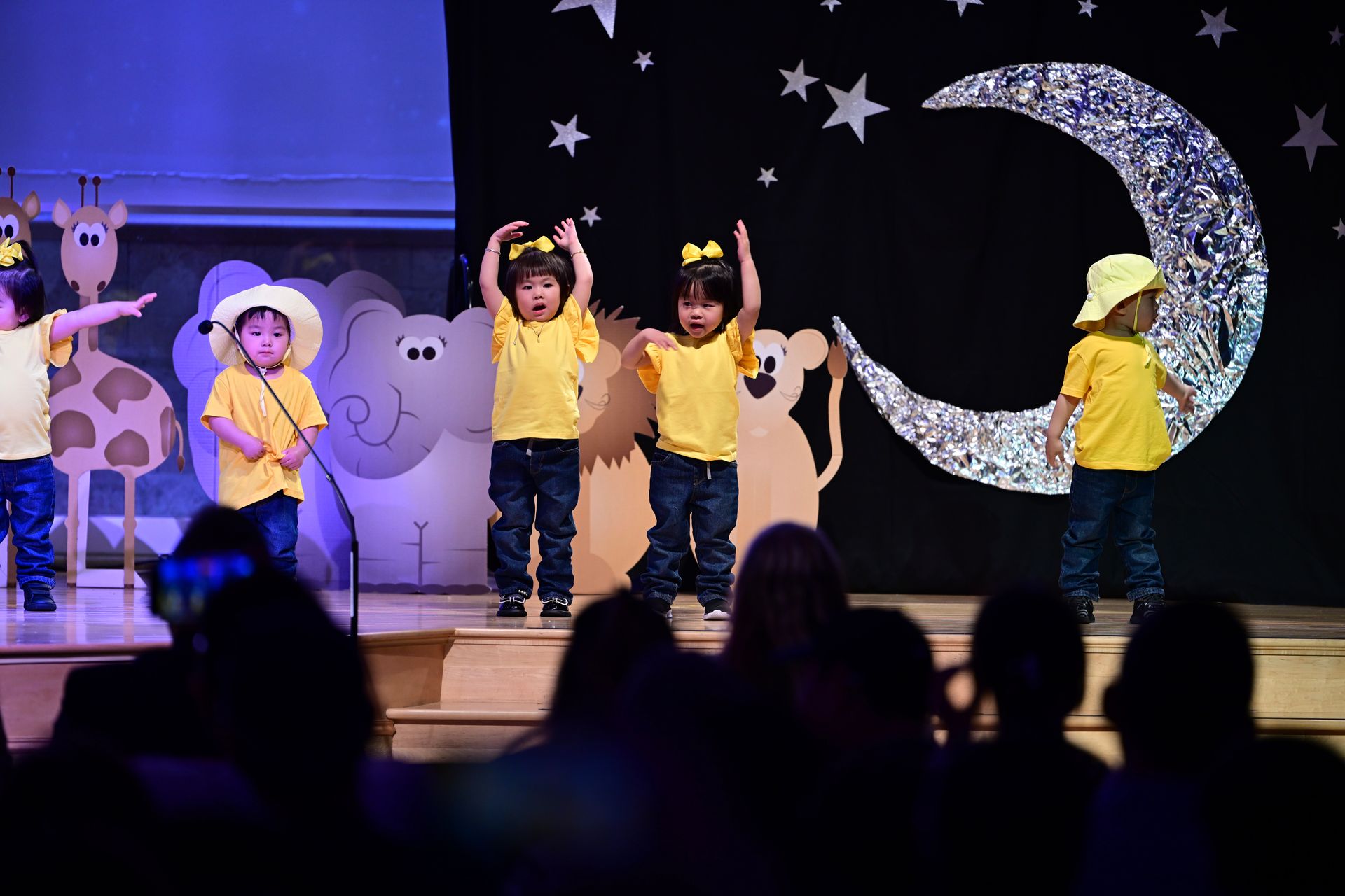 Children in yellow shirts and blue jeans perform on stage with a starry night backdrop.