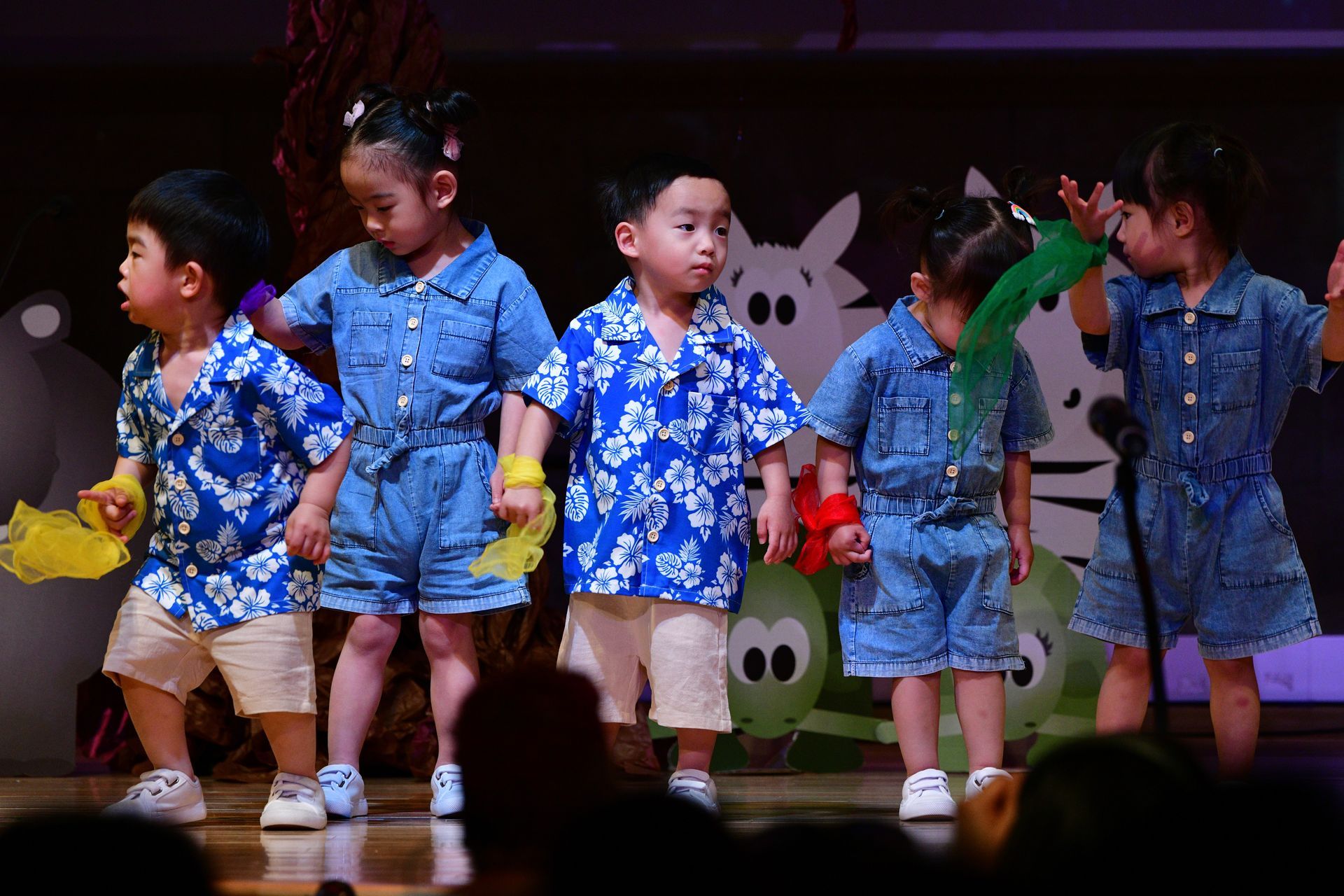 Five children in matching blue outfits performing on stage, some holding props.