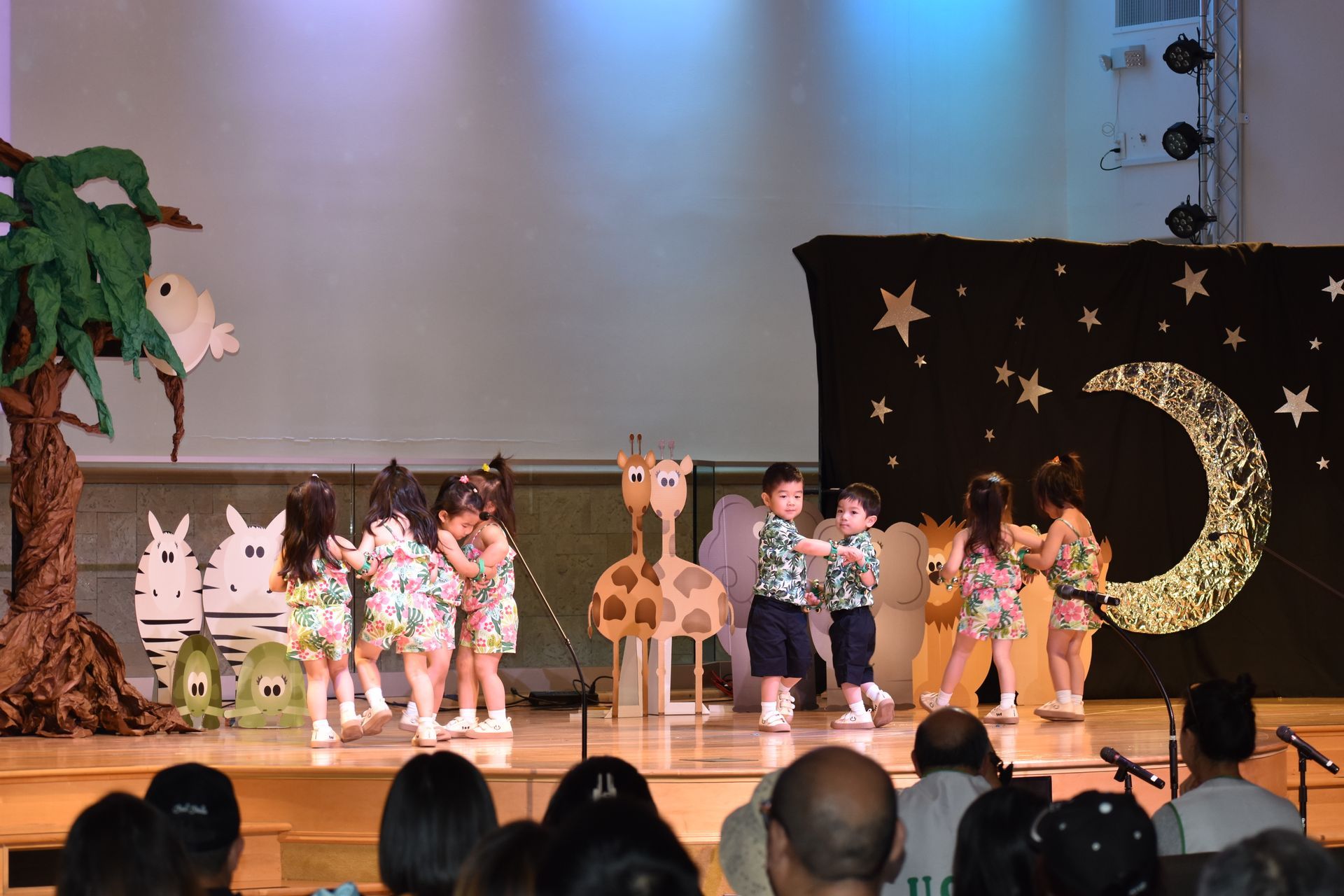 Children in costumes performing on a stage with animal props and backdrop.