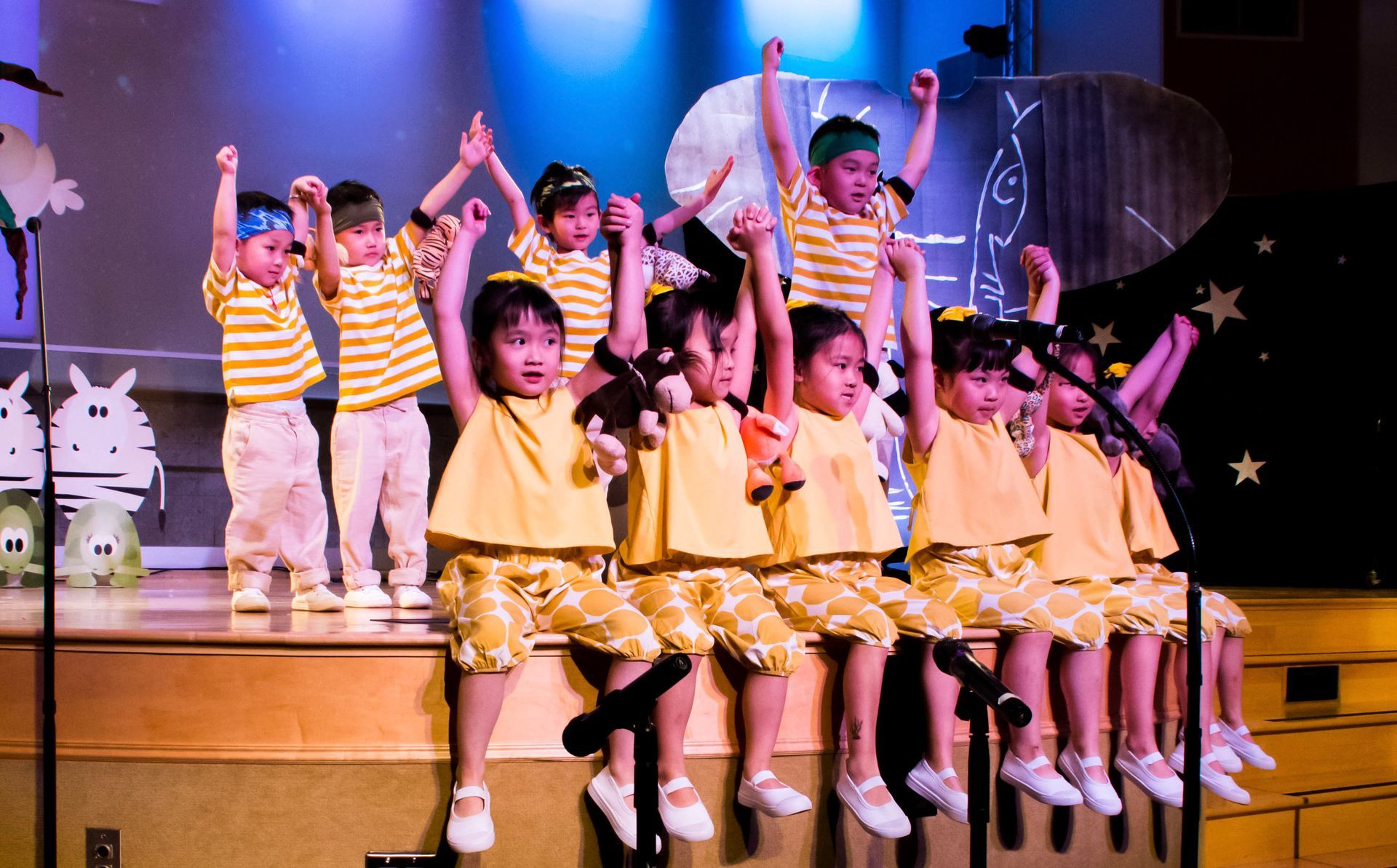 Children in yellow outfits perform on stage with arms raised.