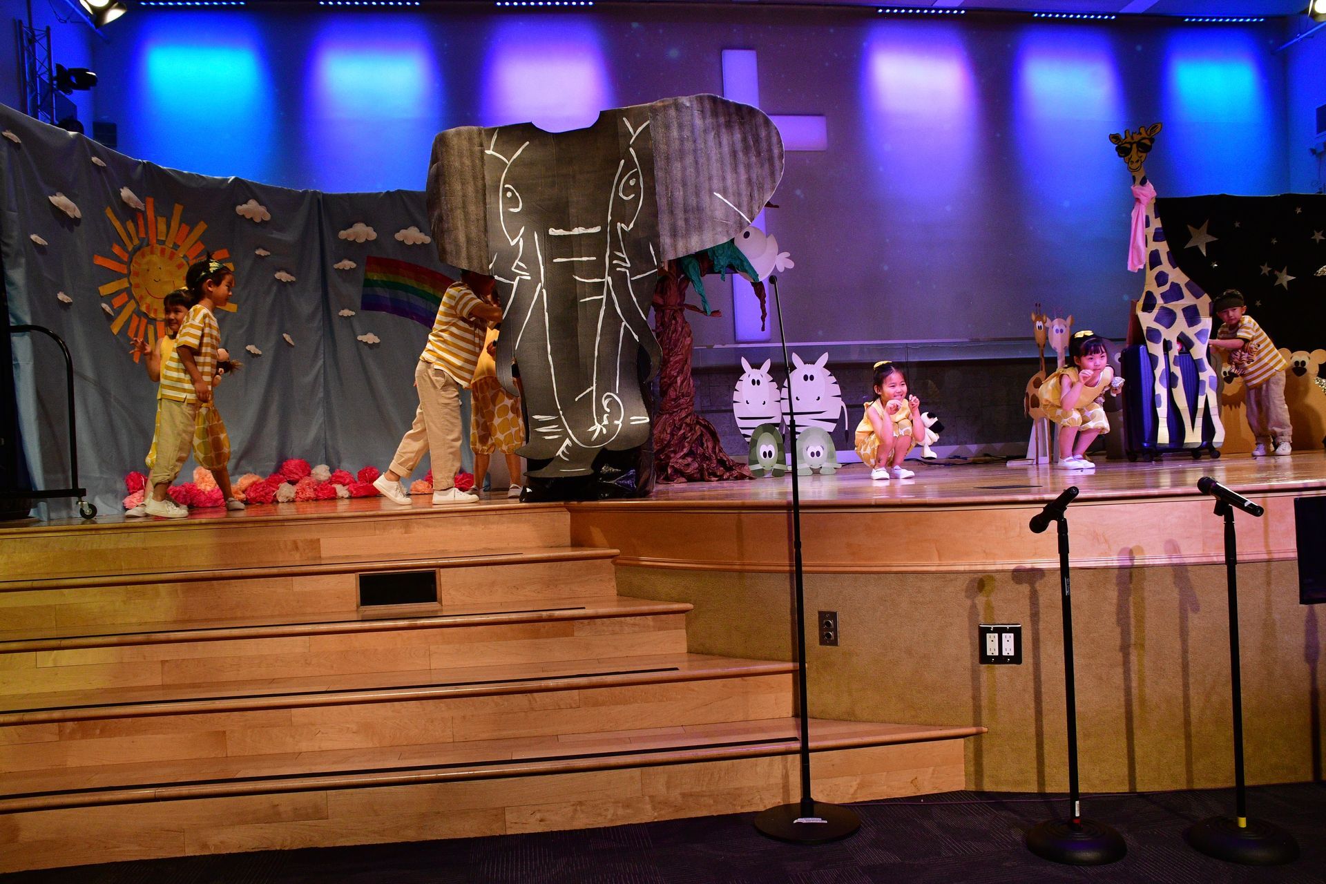 Children's stage production with animal costumes and props on stage. Lit with blue and white lights.