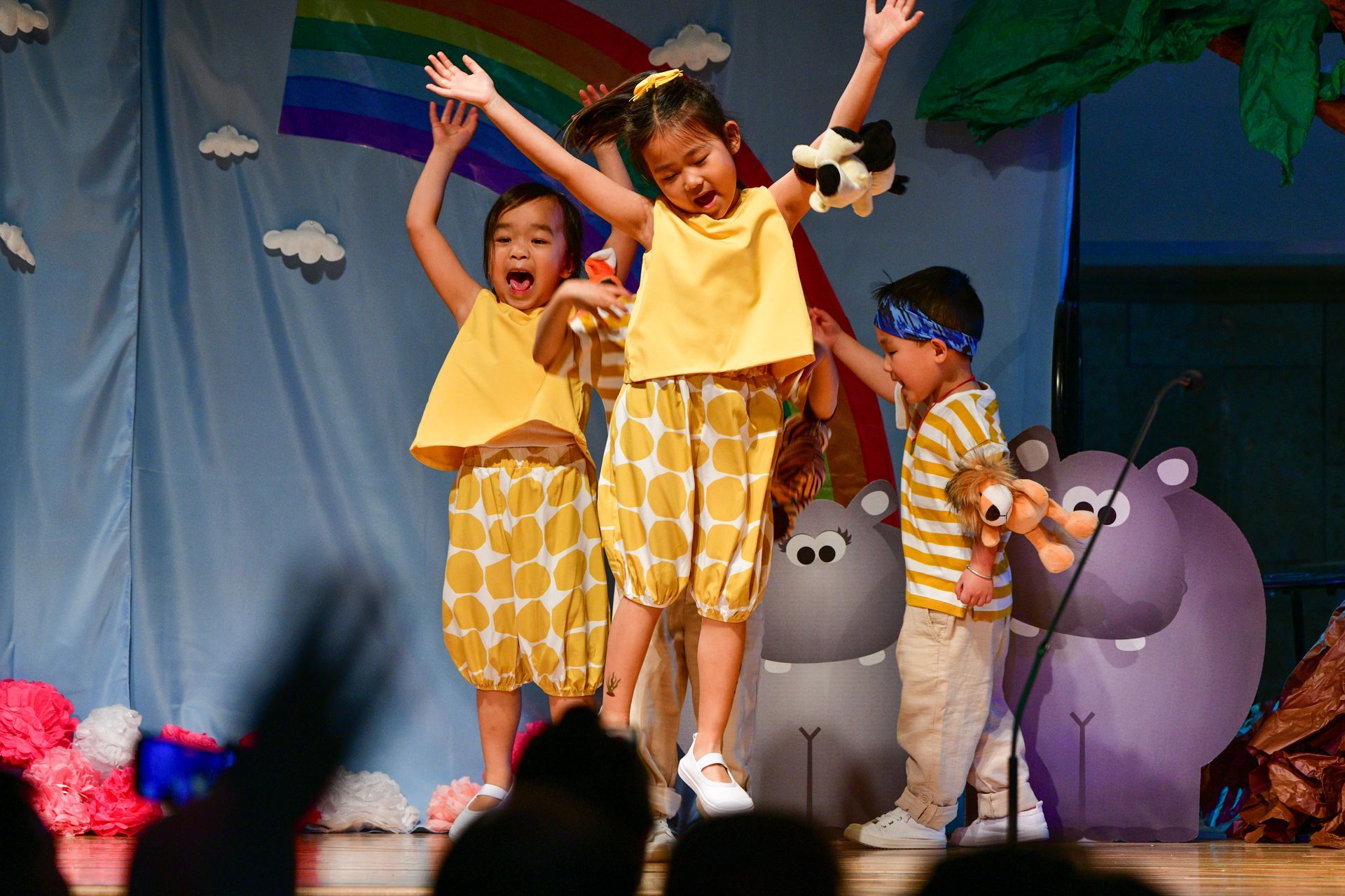 Children performing on stage, wearing yellow, with props.