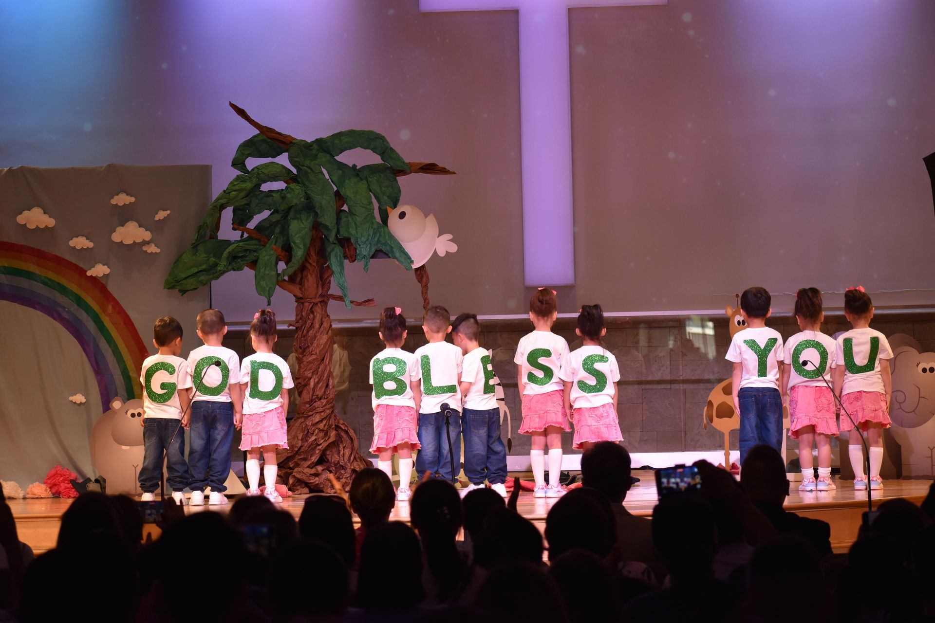 Children on stage in a church play. Shirts spell 