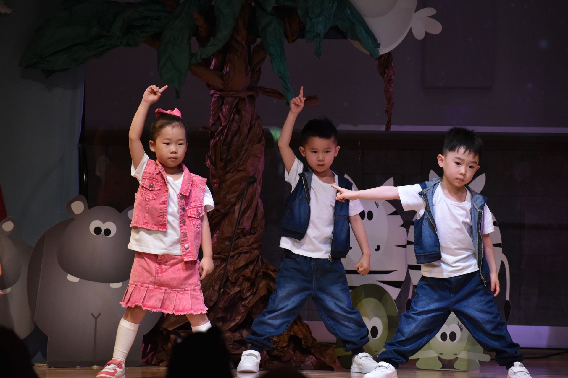 Children performing on stage, wearing denim vests and white shirts.