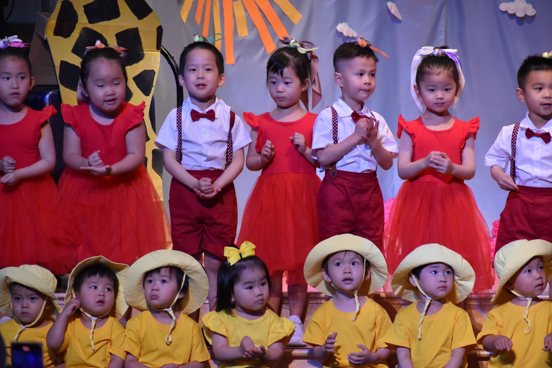 Children in red and yellow outfits perform on stage.