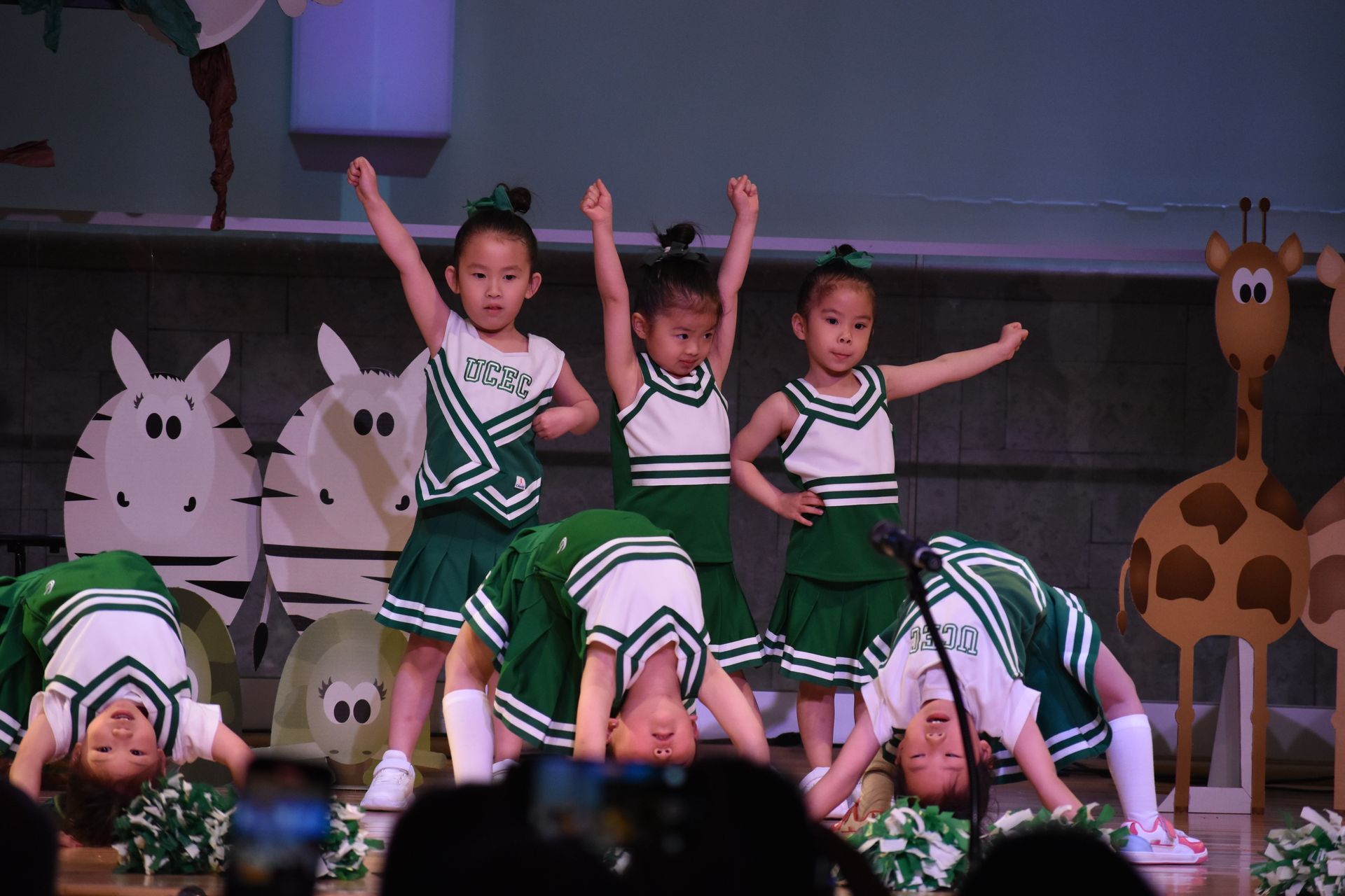 Children in green and white cheerleading outfits performing on stage.