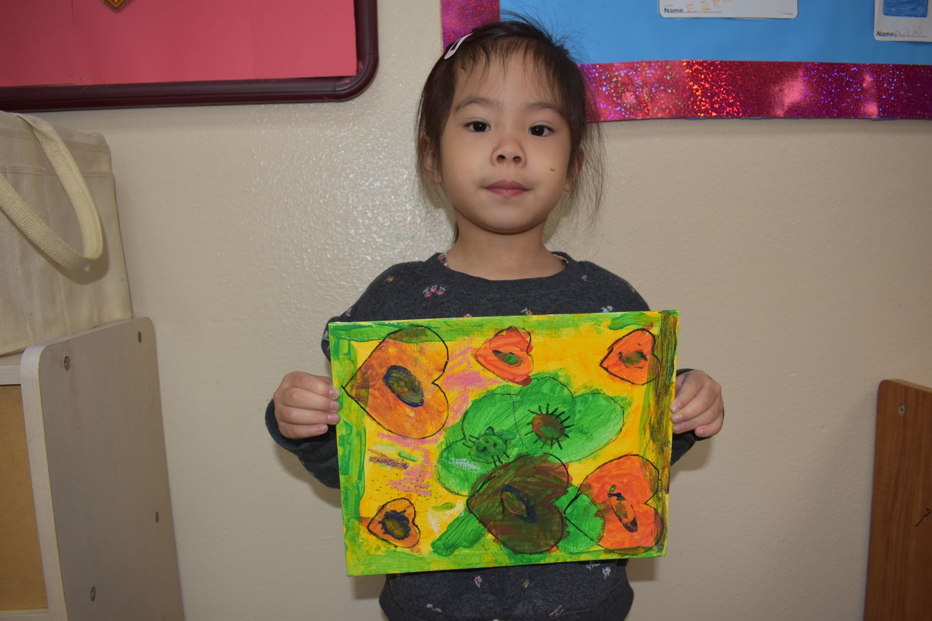 Young child holding colorful artwork with floral designs, smiling.