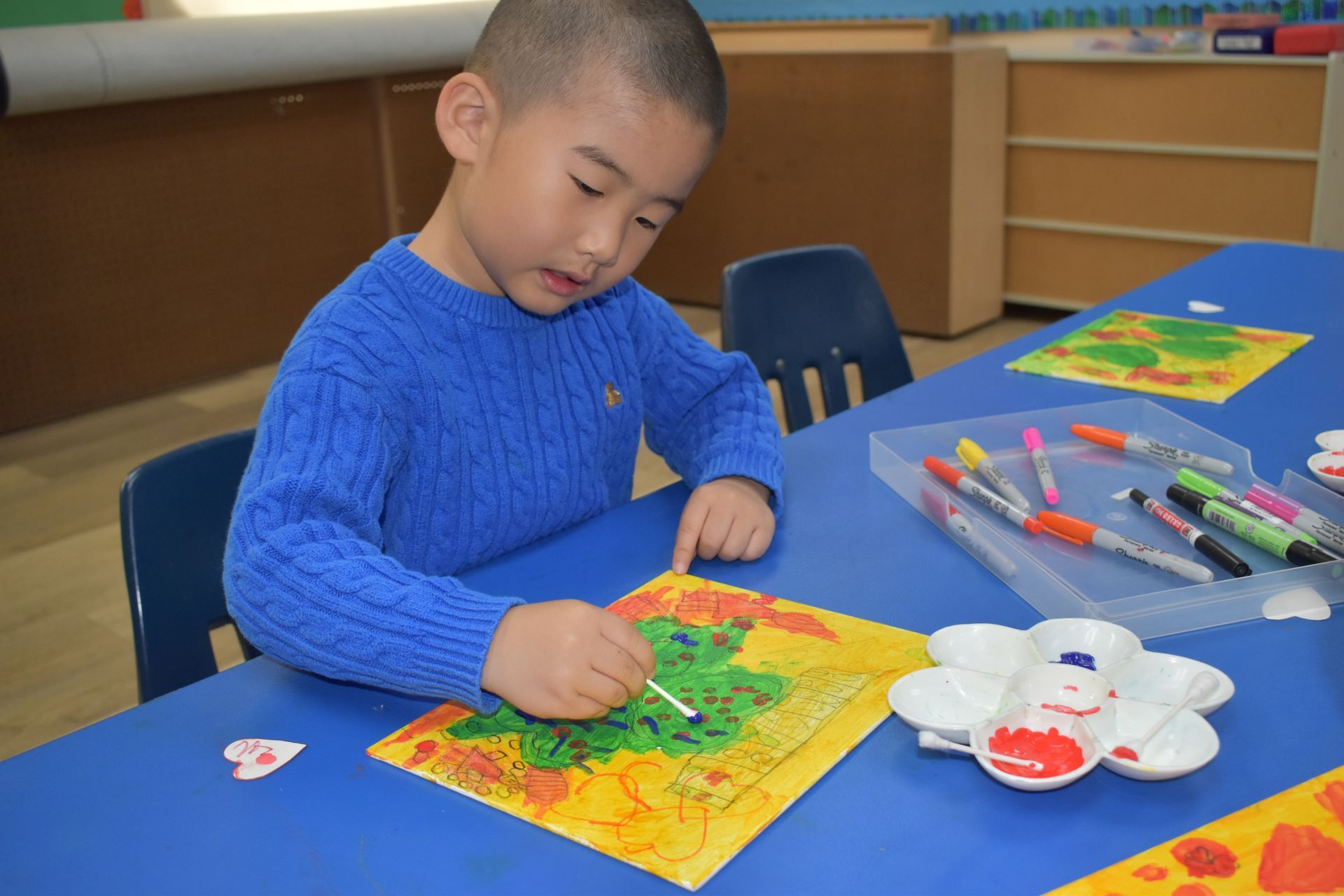 Young child coloring a picture with markers at a table.
