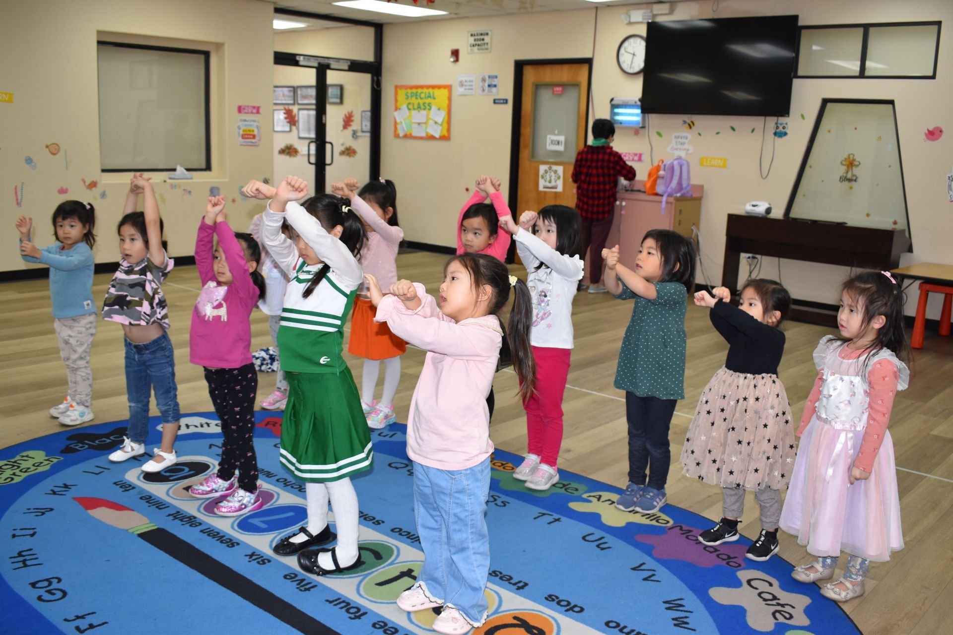 Children in a classroom doing a coordinated arm exercise on a circular rug.