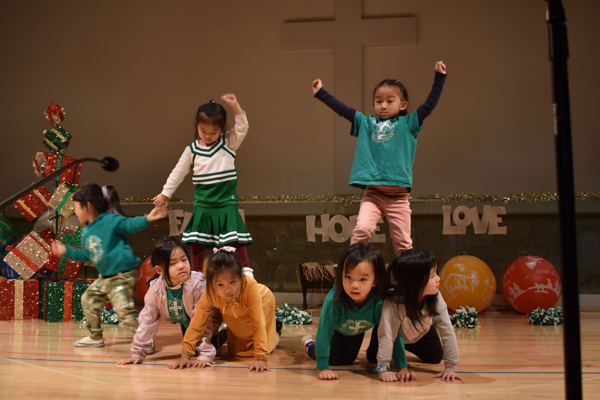 Children on stage performing a pyramid, Christmas decor in the background.