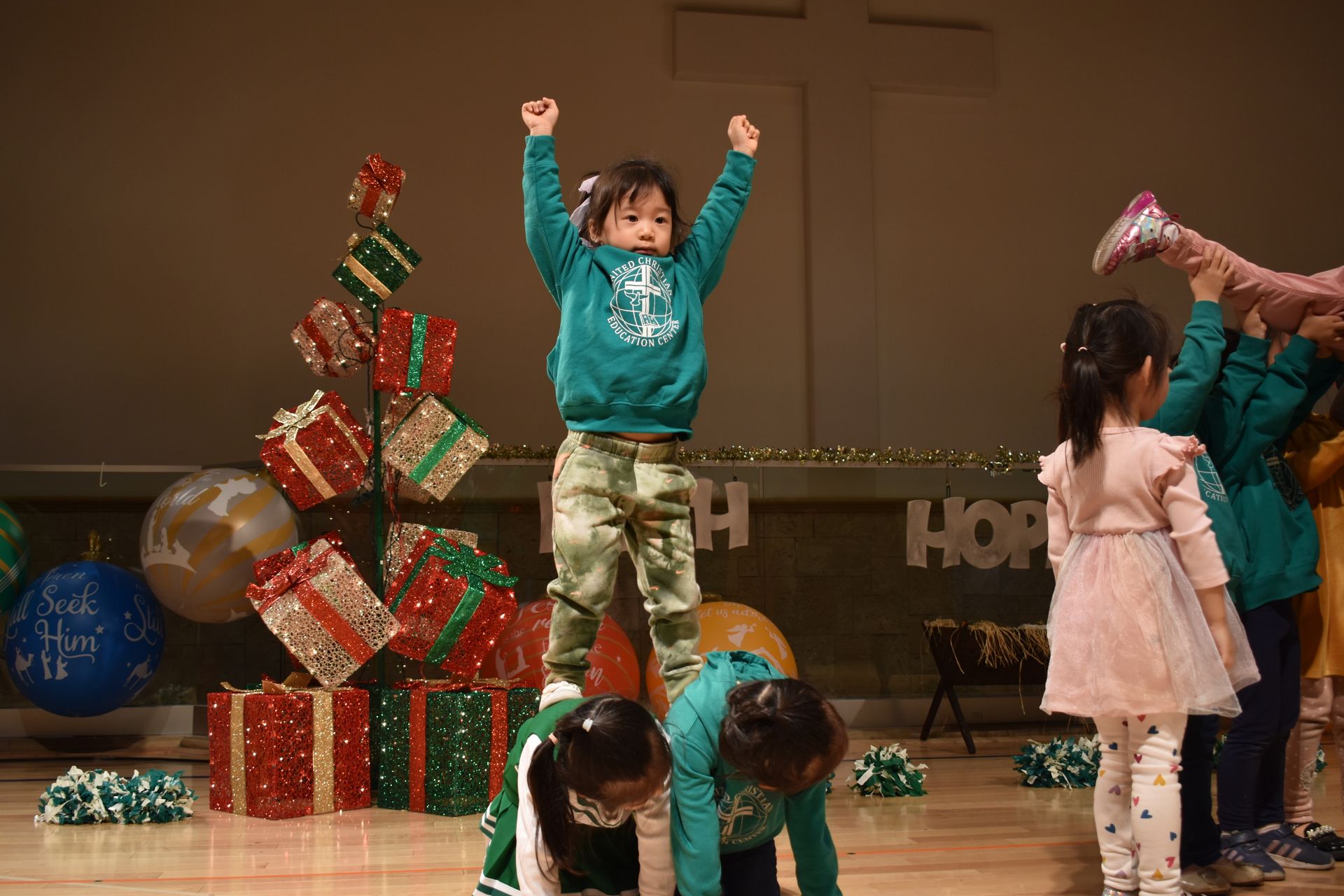 Children performing, one standing atop others. Christmas decorations and stage set visible.