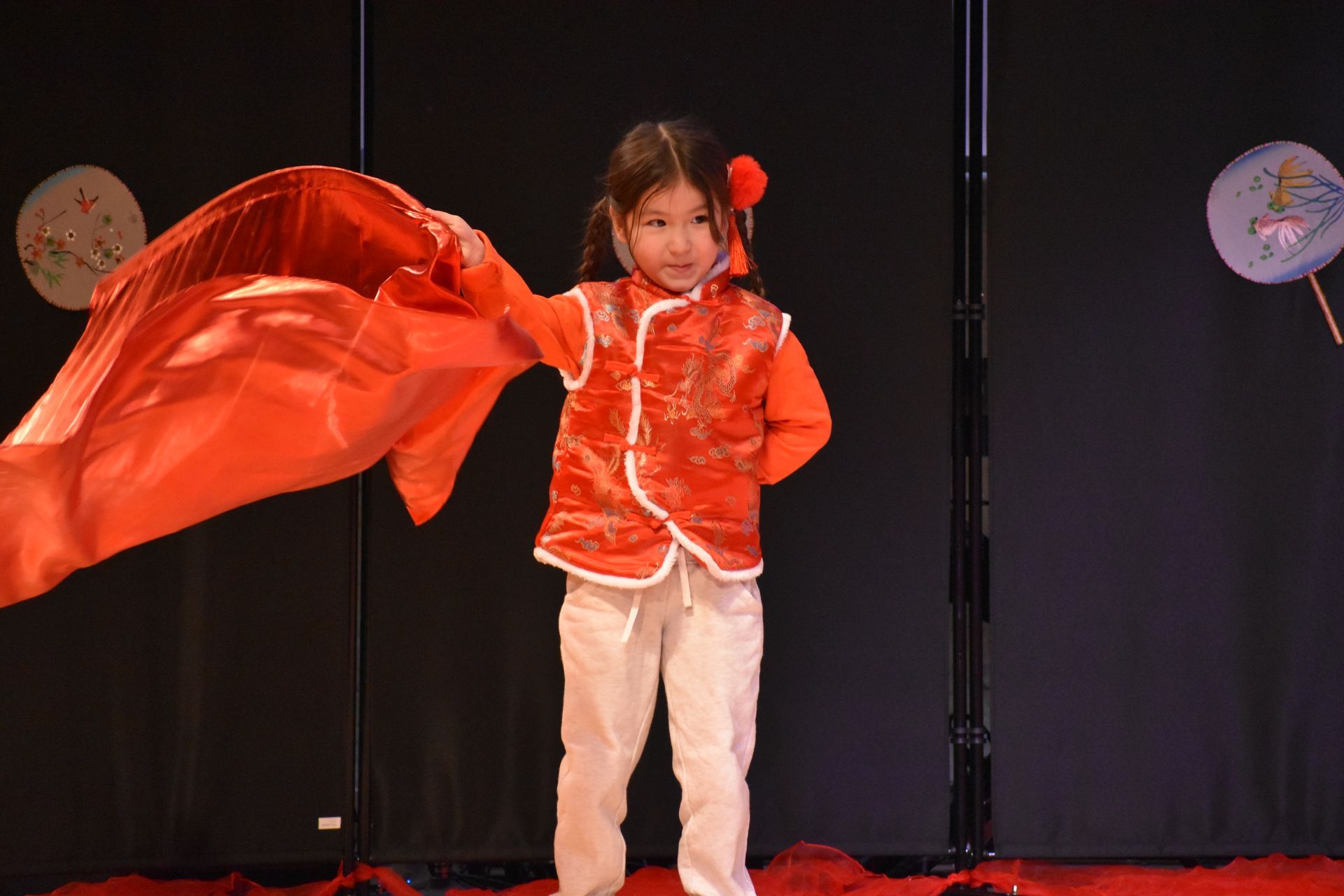 Young child in red traditional clothing performing on stage, holding a red cloth.