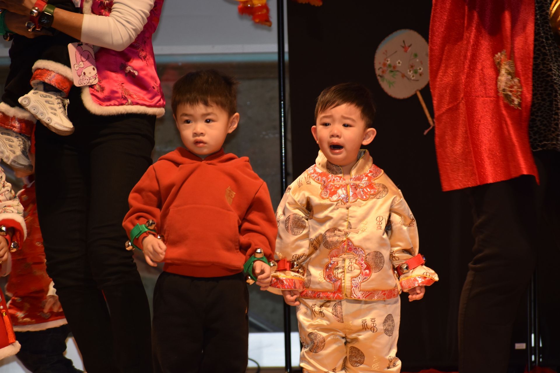 Two young children on stage, one in red, the other in ornate gold, with open mouth, as part of a performance.