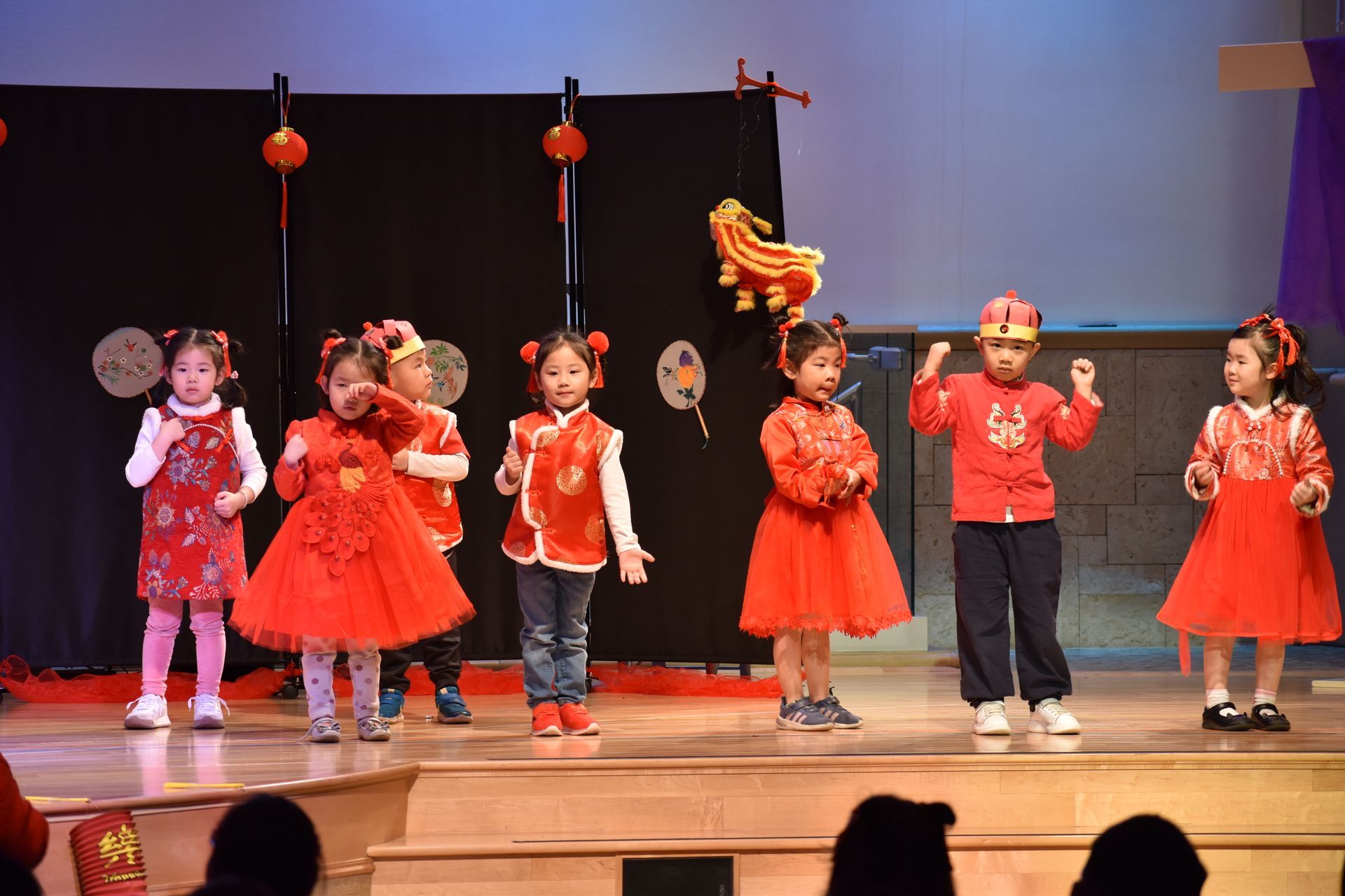 Children in red and white outfits perform a dance on stage. Decorations and lanterns are visible.