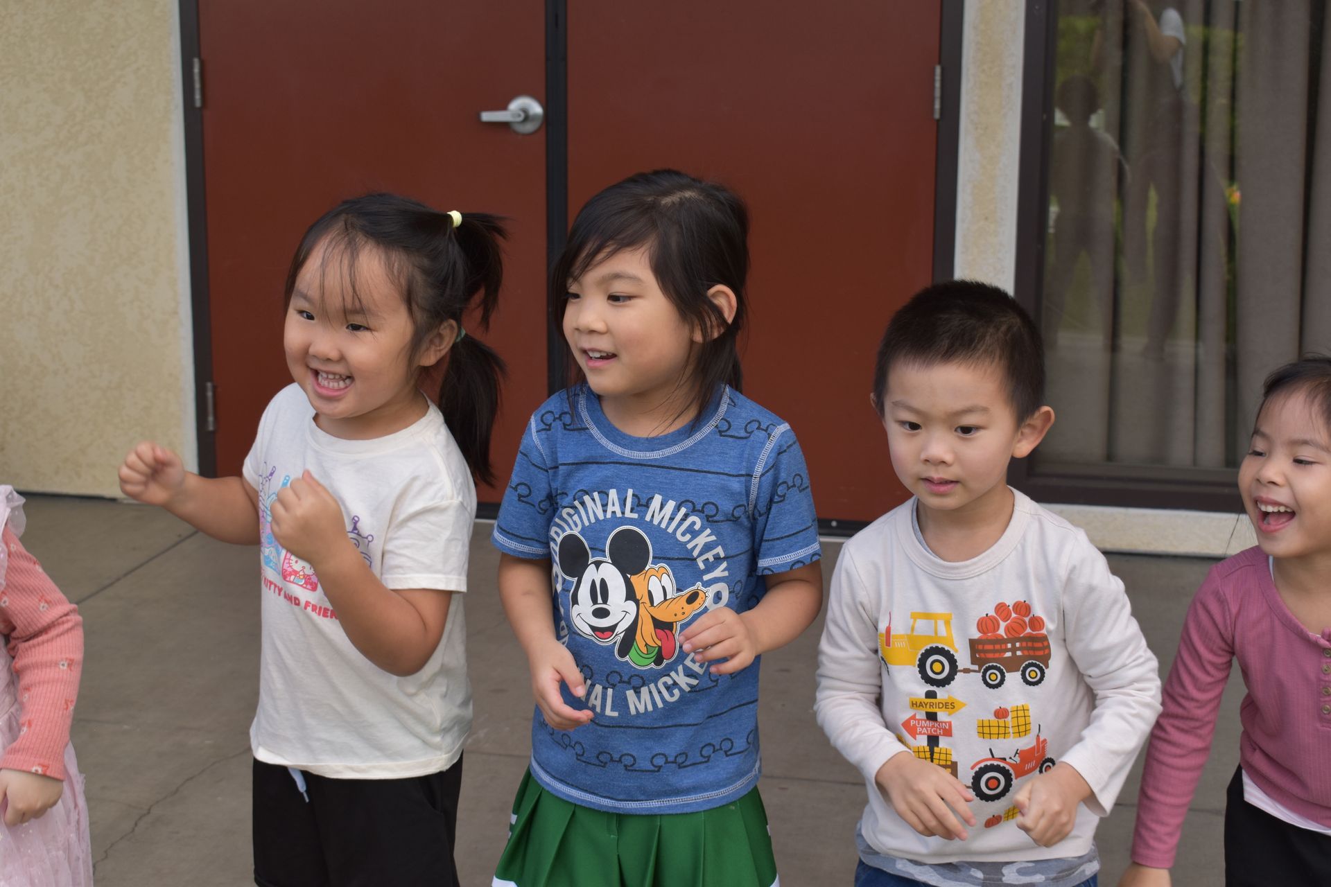Five children smiling and laughing outdoors. They appear to be in a group, possibly playing.
