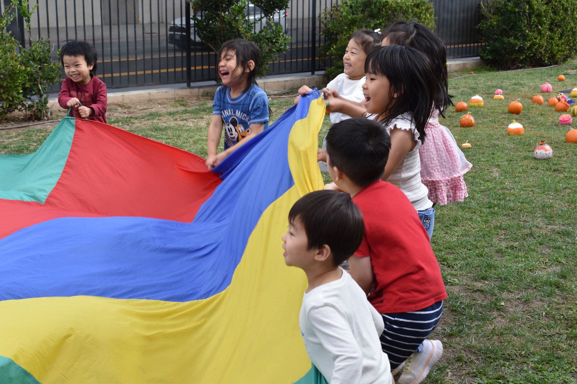 Children playing with a colorful parachute on a grassy field, smiling and lifting the fabric.