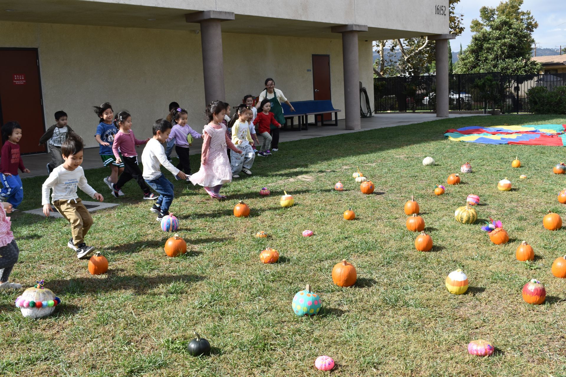 Children running and playing on a lawn dotted with pumpkins.