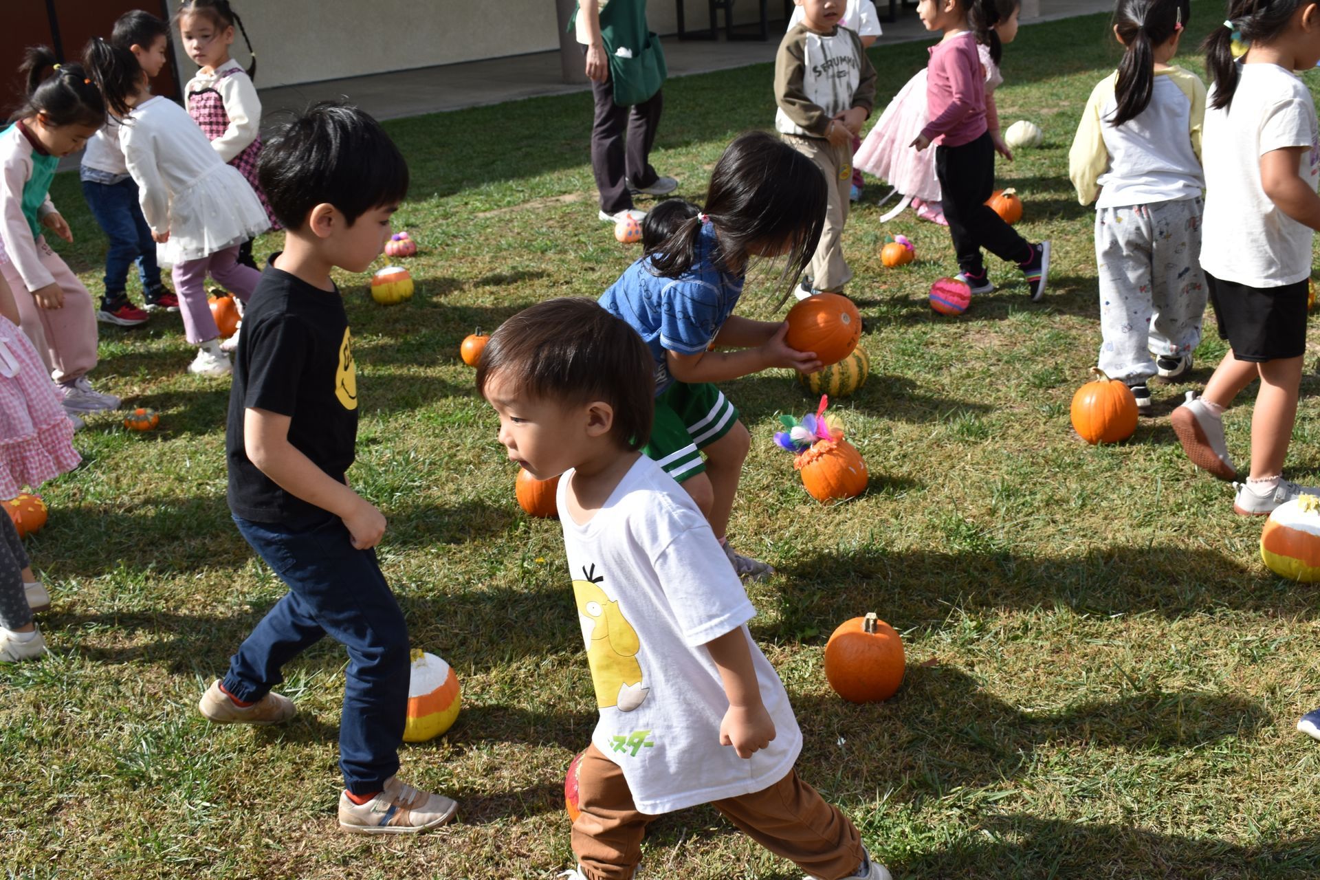 Children on a grassy field, some holding pumpkins, possibly playing a game.