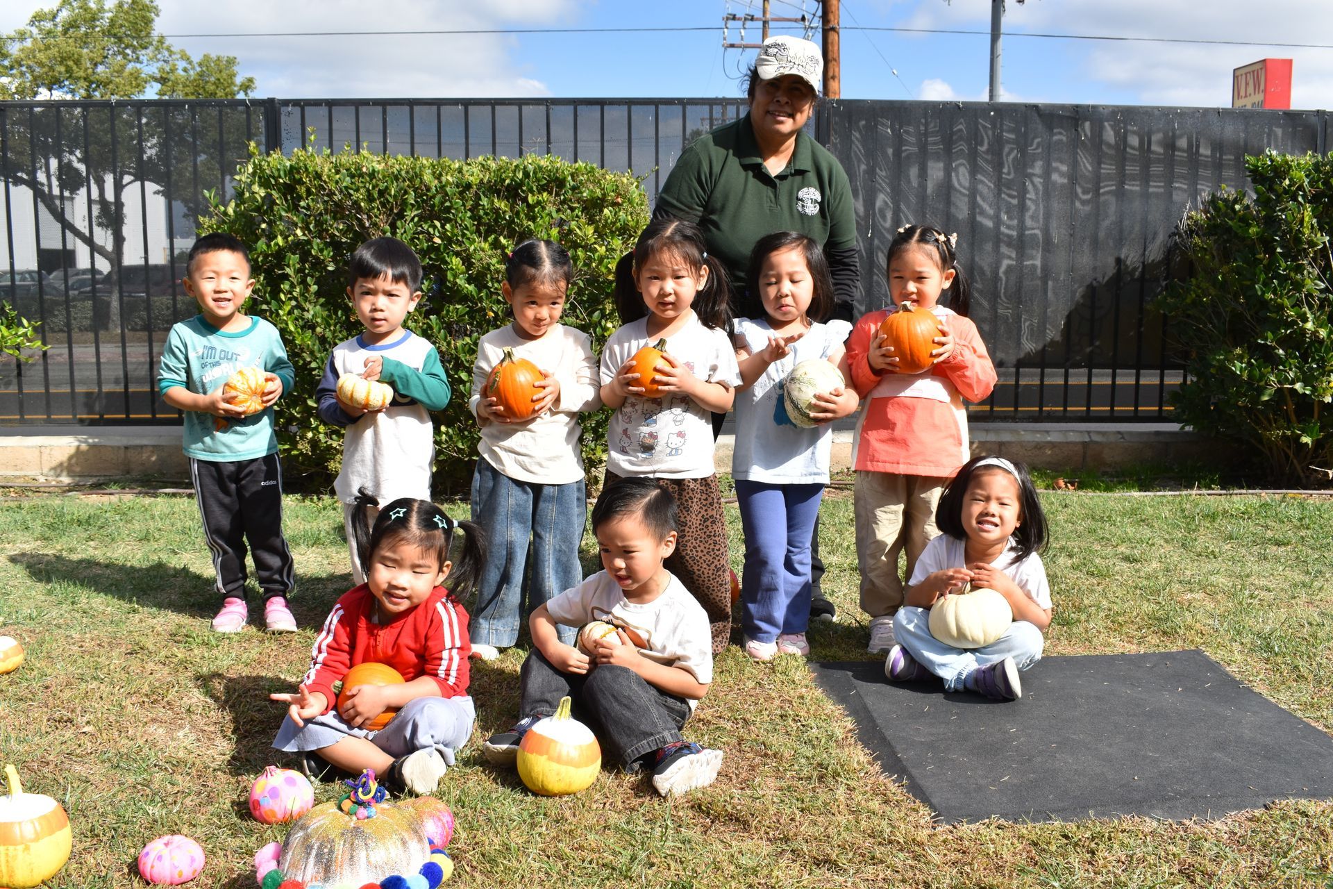 Group of children and adult with pumpkins outdoors. Children holding pumpkins, smiling.