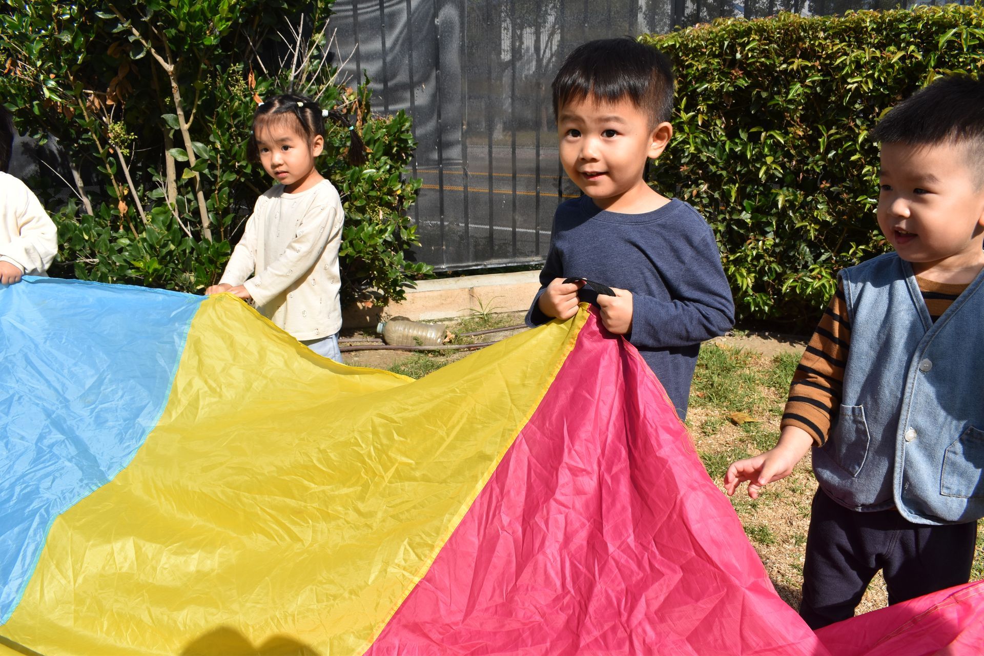 Children playing with a colorful parachute outside; sunny day.
