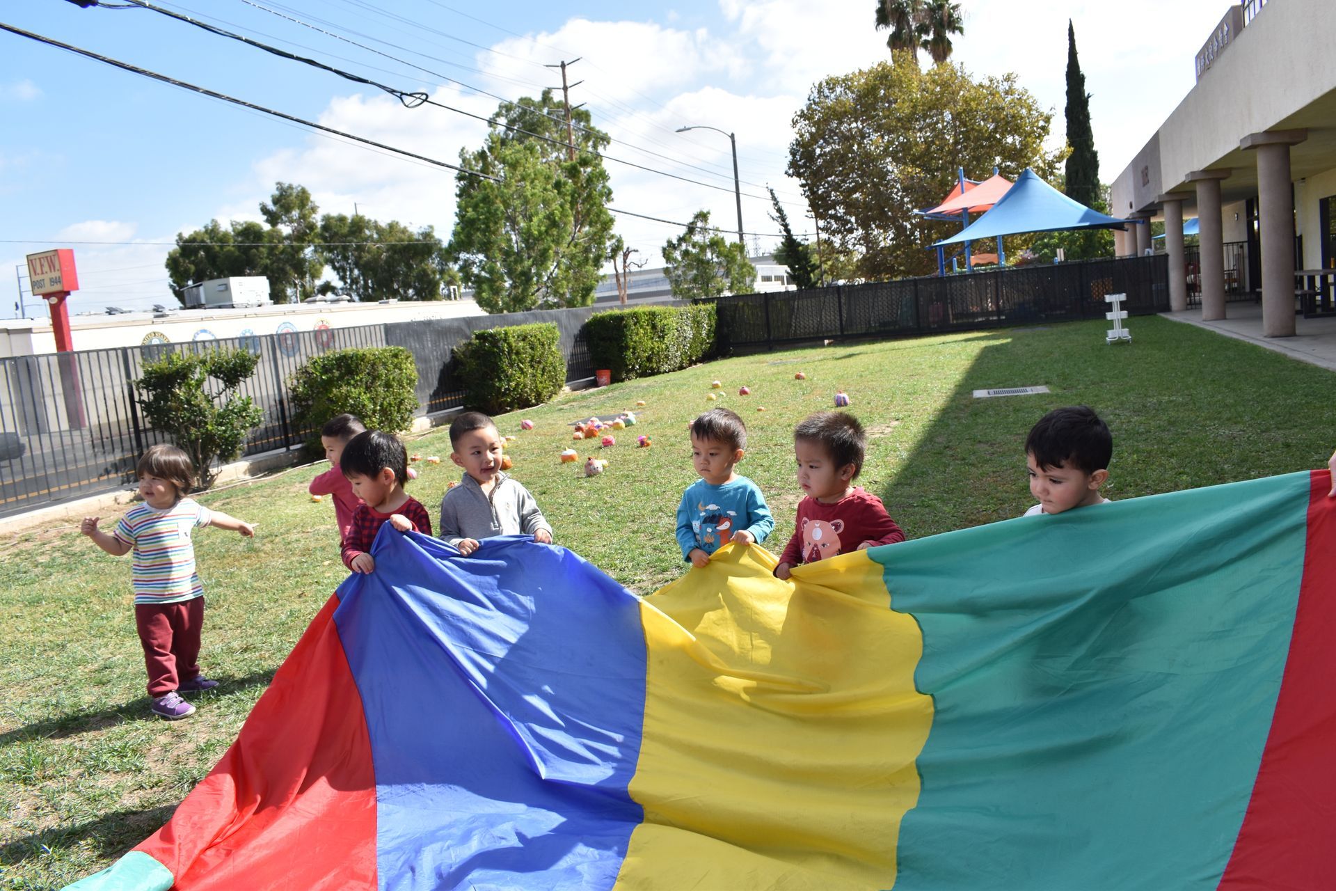 Children playing with a colorful parachute on a grassy lawn outdoors.