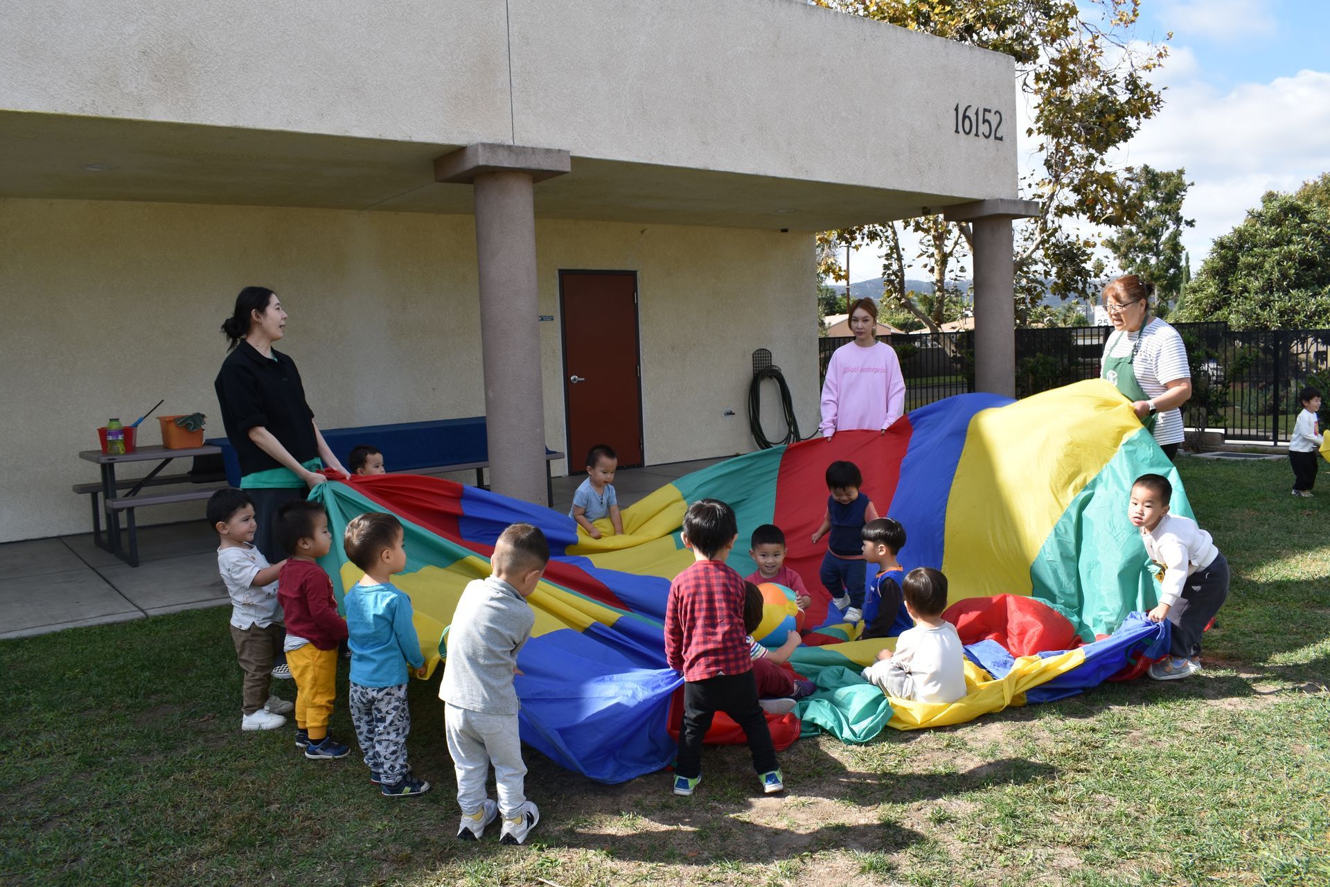 Children and adults playing with a colorful parachute outside a building.