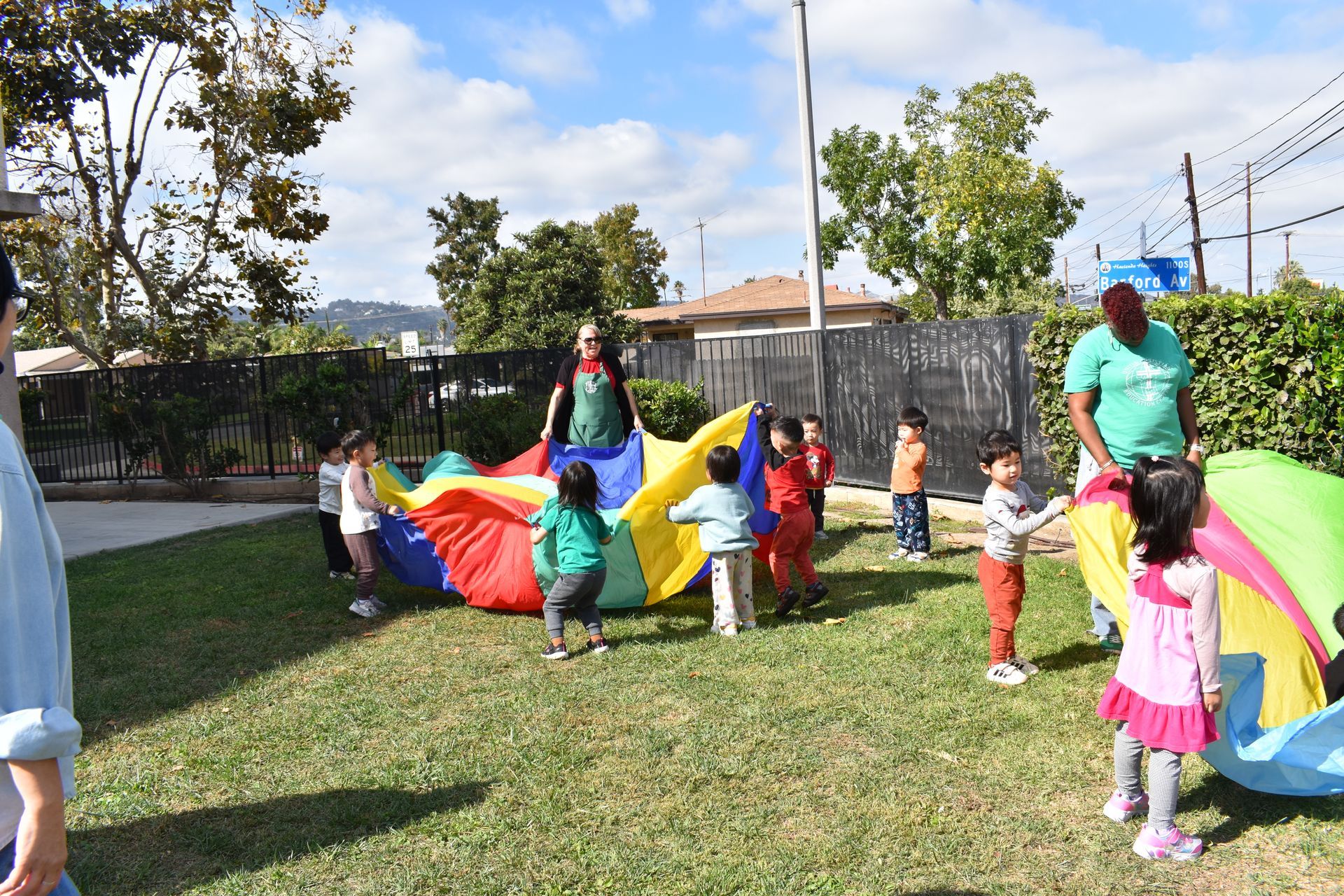 Children and adults playing with a colorful parachute on a grassy lawn.