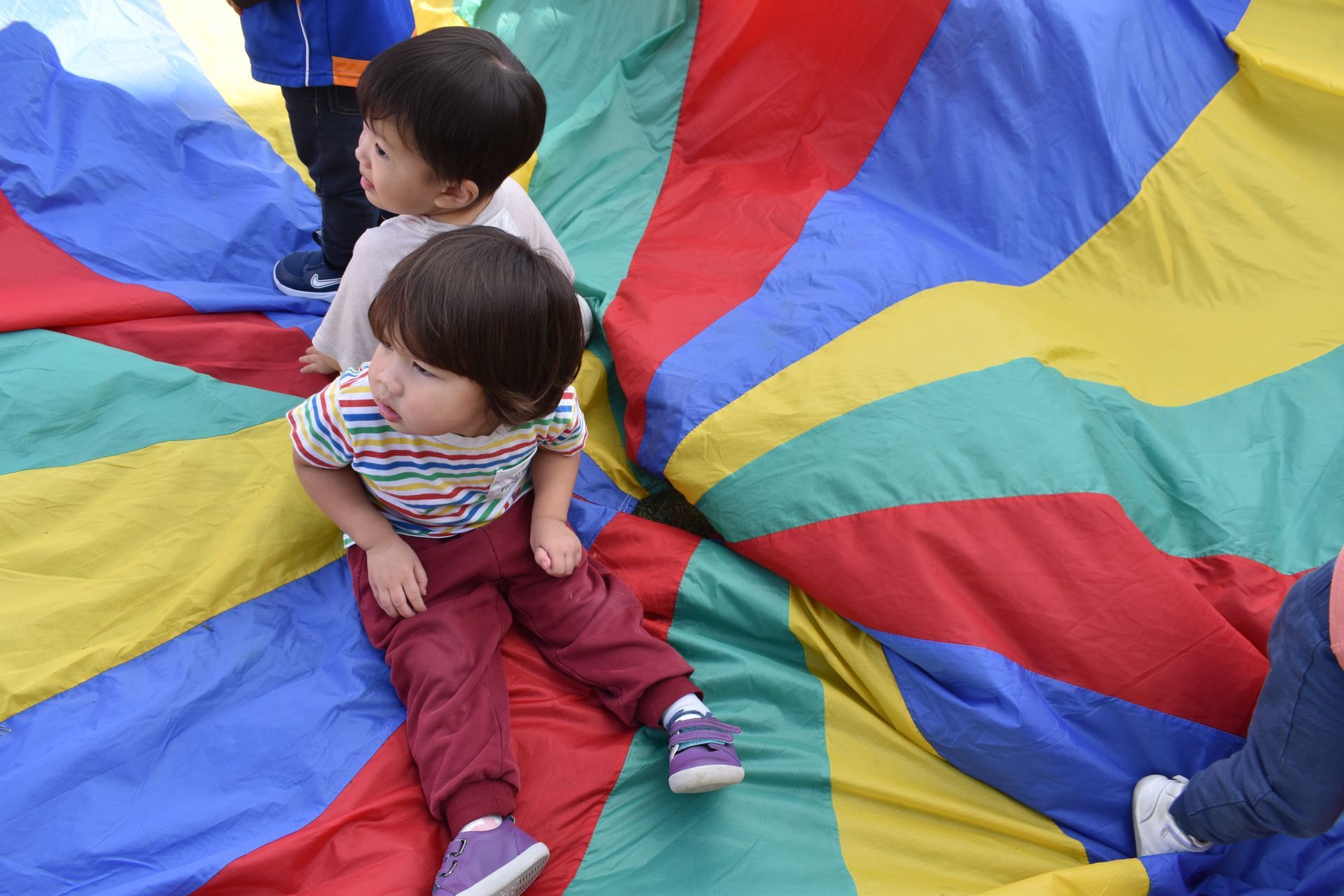Children sit on a large, colorful parachute, looking around.