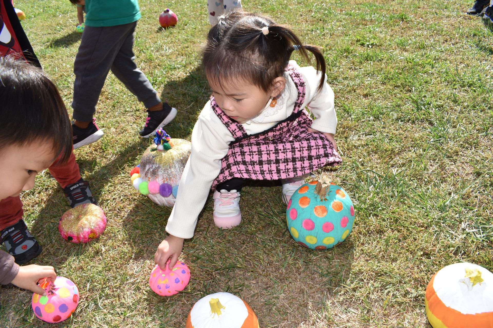 Children playing outdoors, reaching for colorful, decorated balls in the grass.