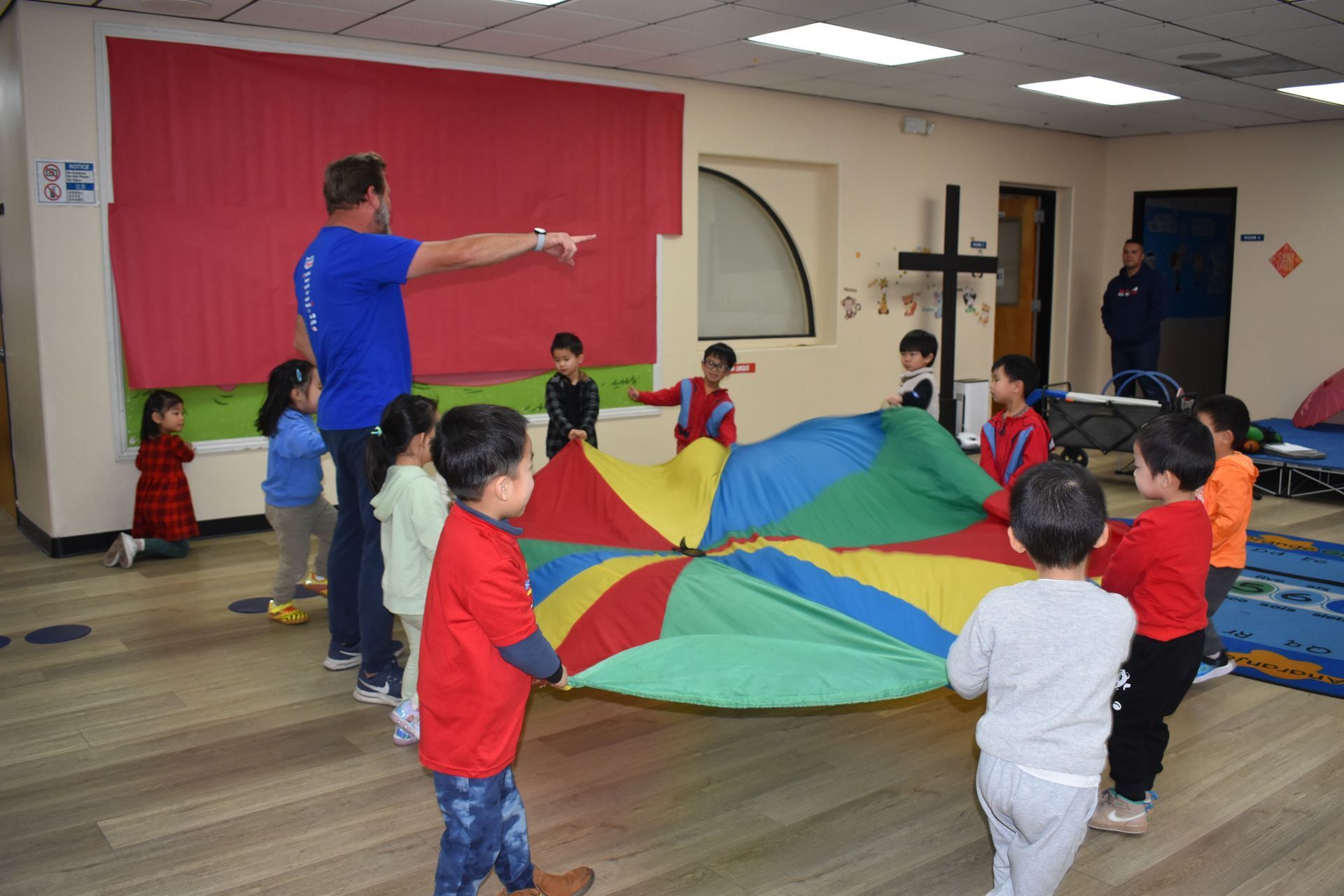 Children and adult playing with a parachute in a room with a red wall.