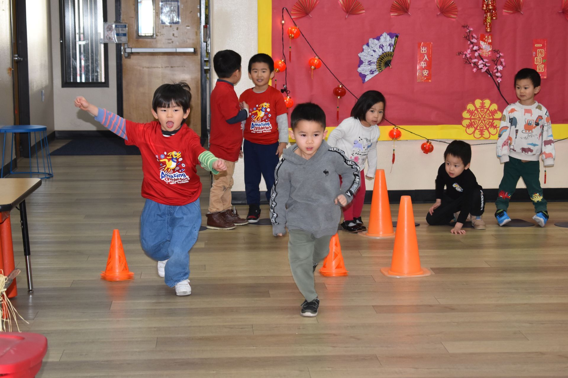 Children playing a game with cones indoors; one child throws a ball with excitement.
