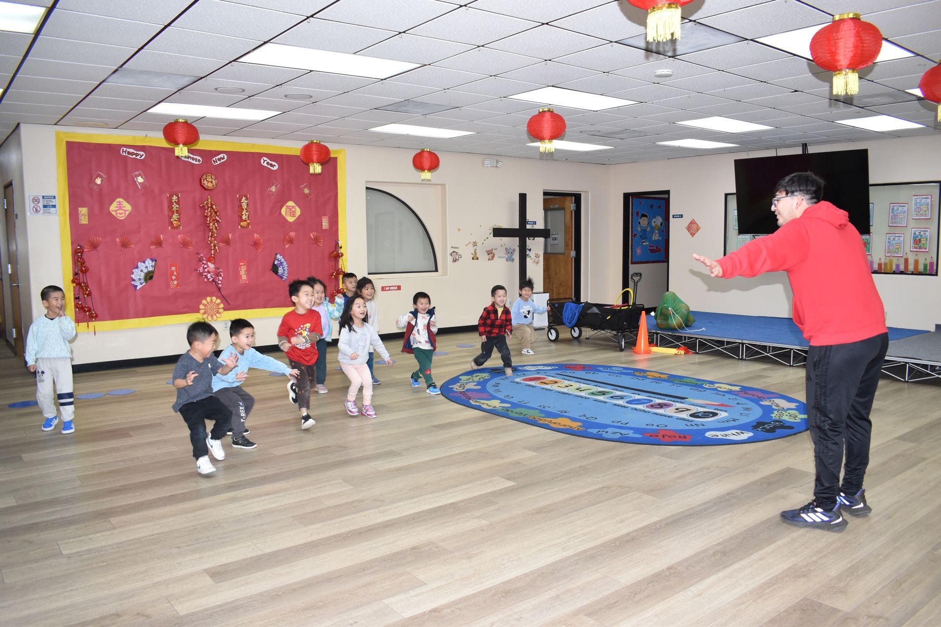 Children running toward a teacher with arms outstretched in a decorated room.