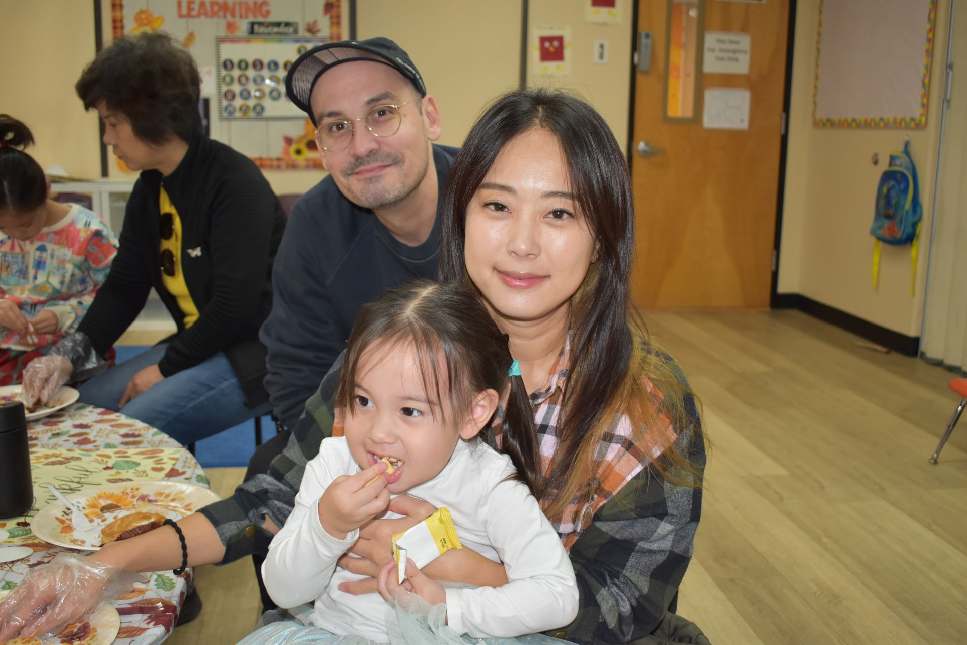 Family indoors: parents with a child at a table, smiling.