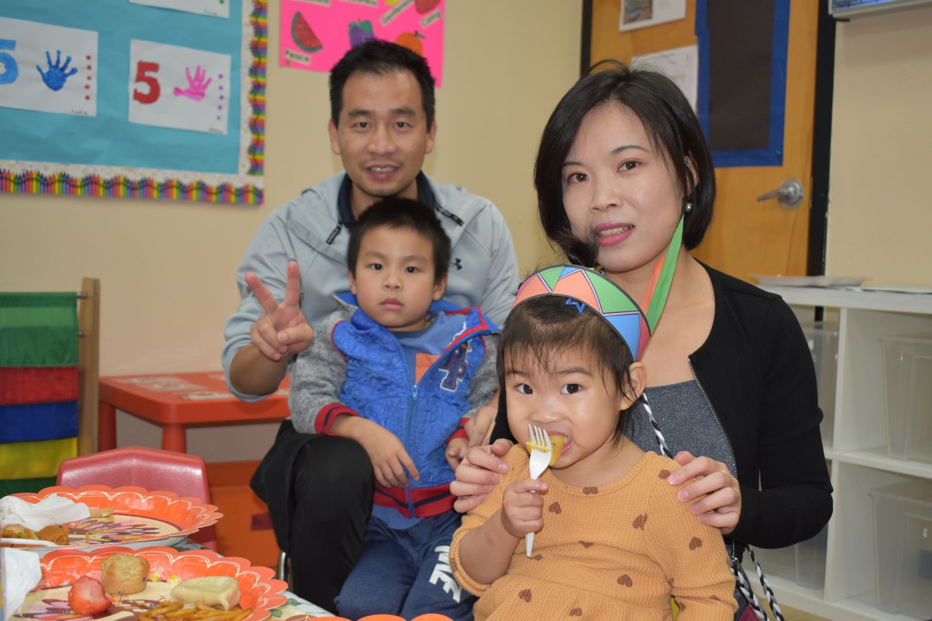 Family with two young children at a birthday party, smiling, cake present.