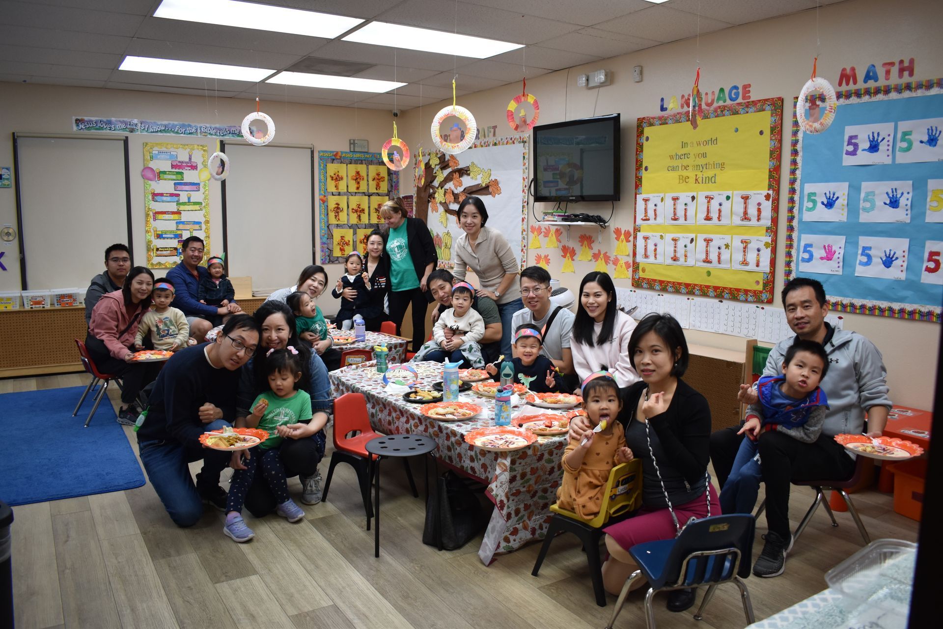 Group of people gathered around a table with food in a classroom setting.