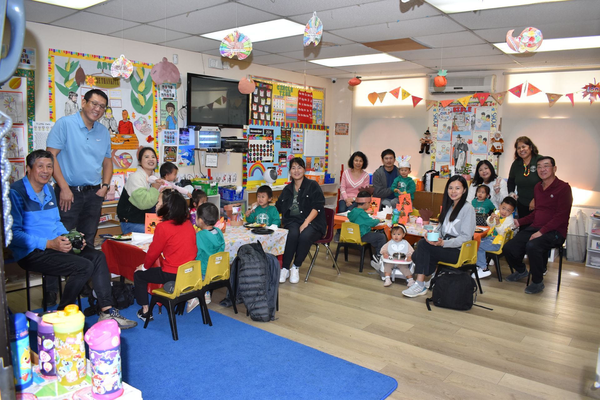 People and children at a colorful party inside a decorated room with tables, balloons, and decorations.