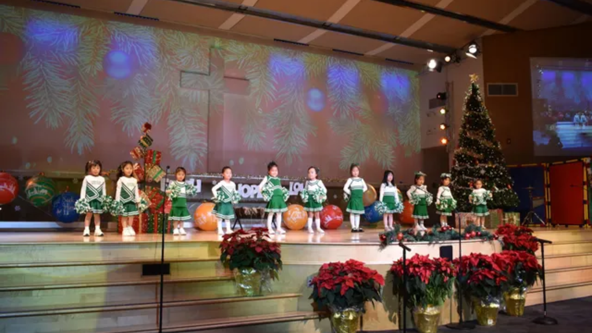 Children in green and white costumes perform on stage with Christmas decorations.