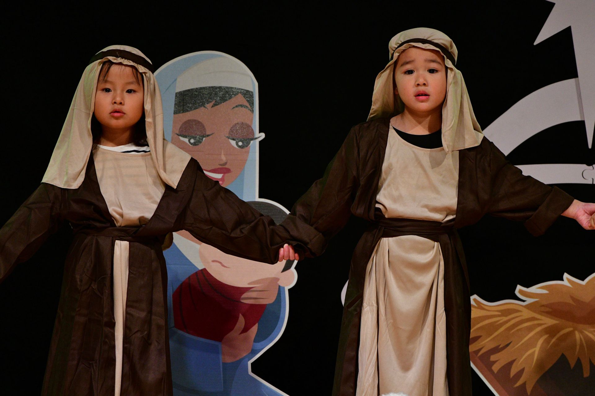 Children in costumes perform in front of a backdrop depicting Mary and baby Jesus.