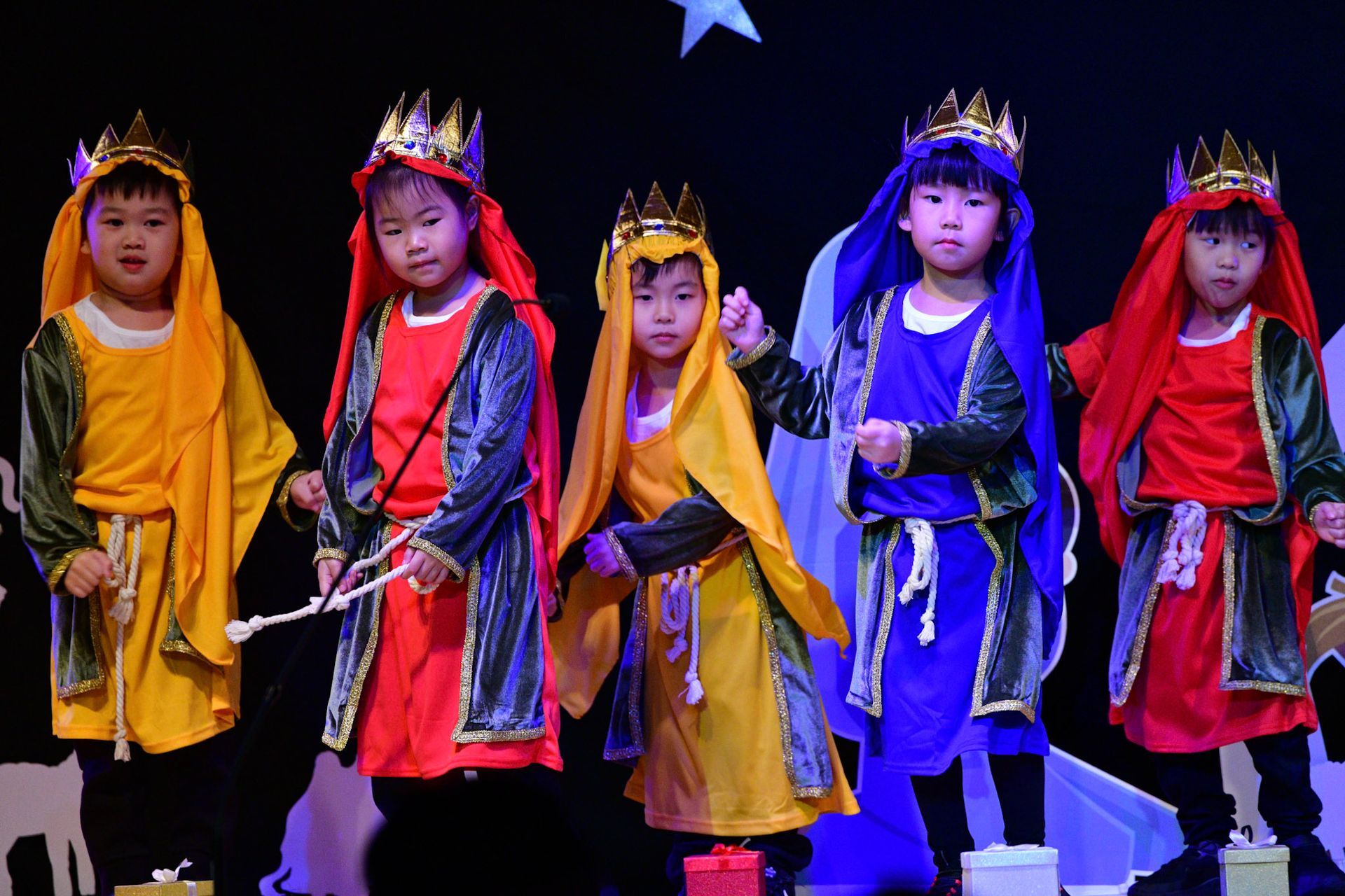 Children in colorful costumes and crowns on stage for a play.