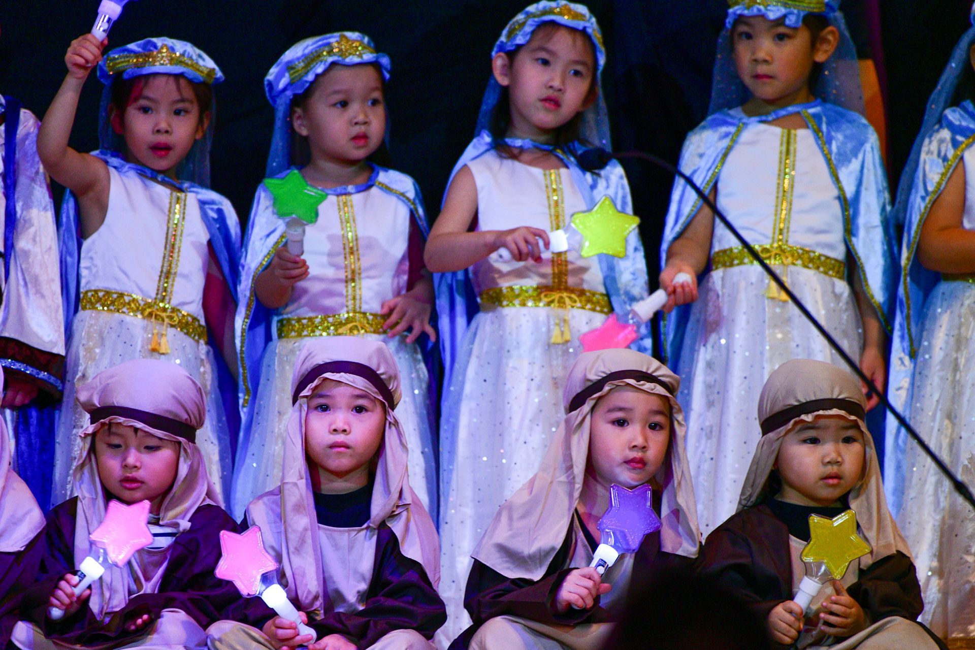 Children in costumes performing on stage, holding star wands.