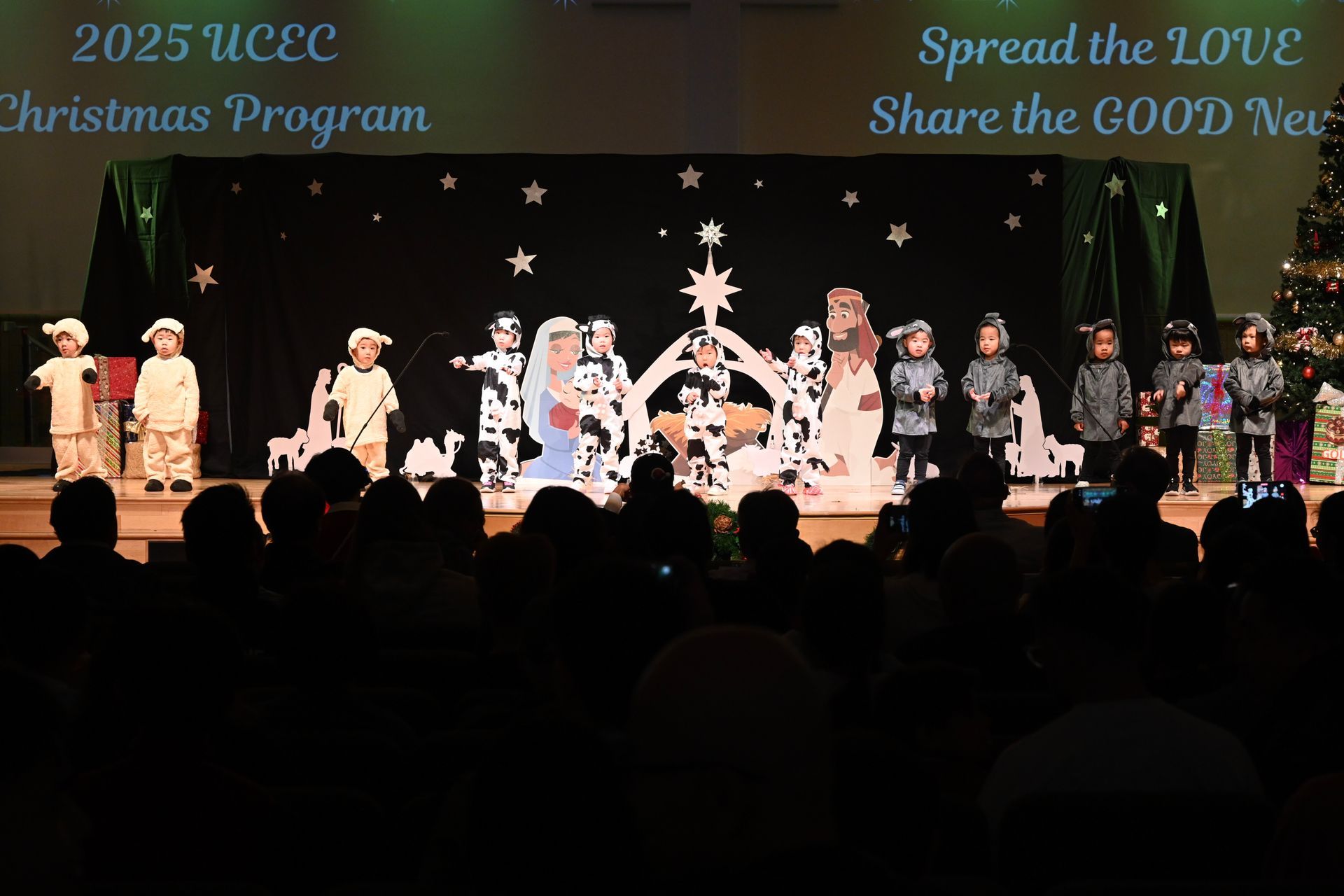 Children performing a nativity play on stage, with audience in the foreground.