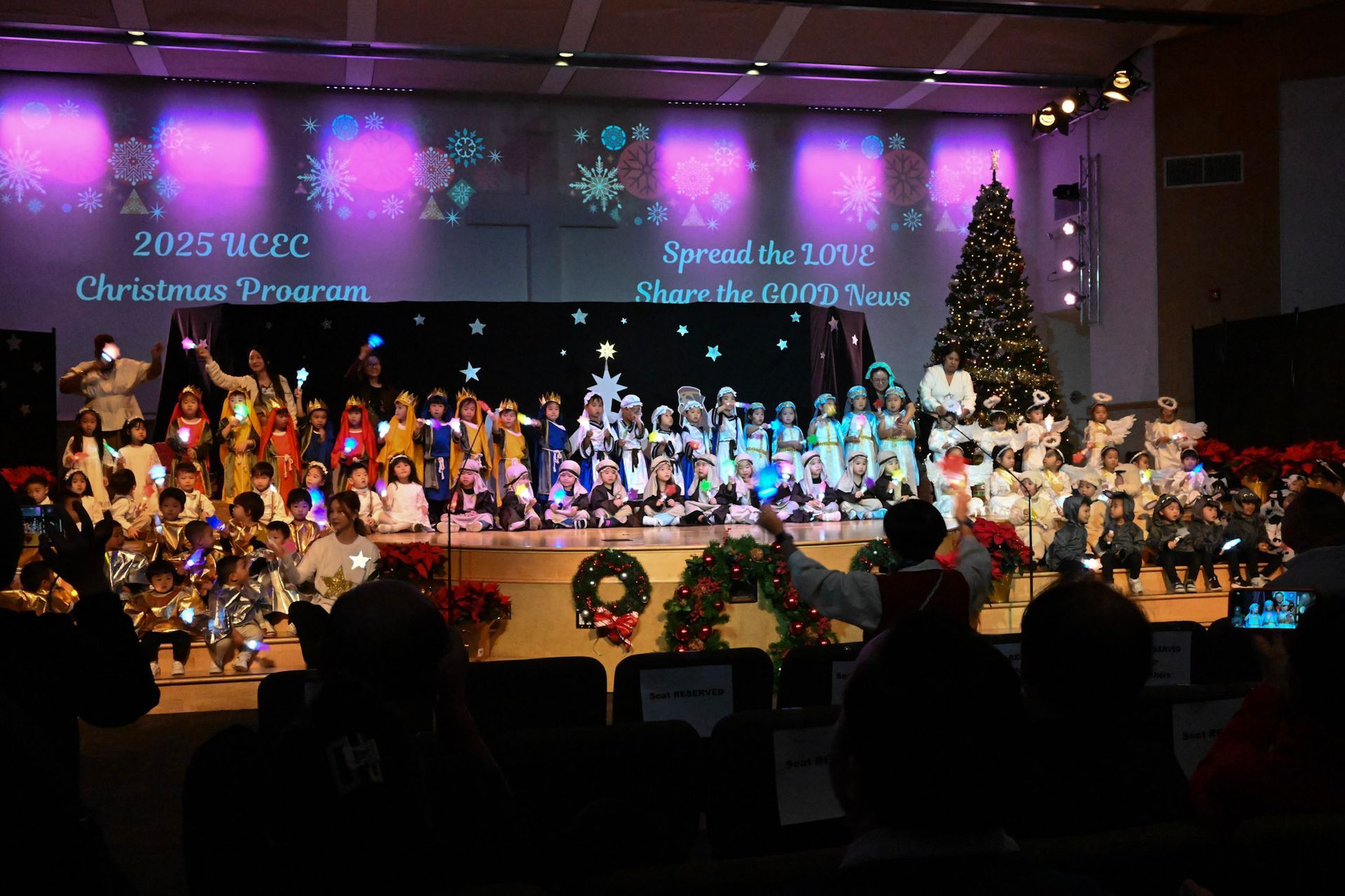 Children on stage for a Christmas program, in front of a Christmas tree and projections.