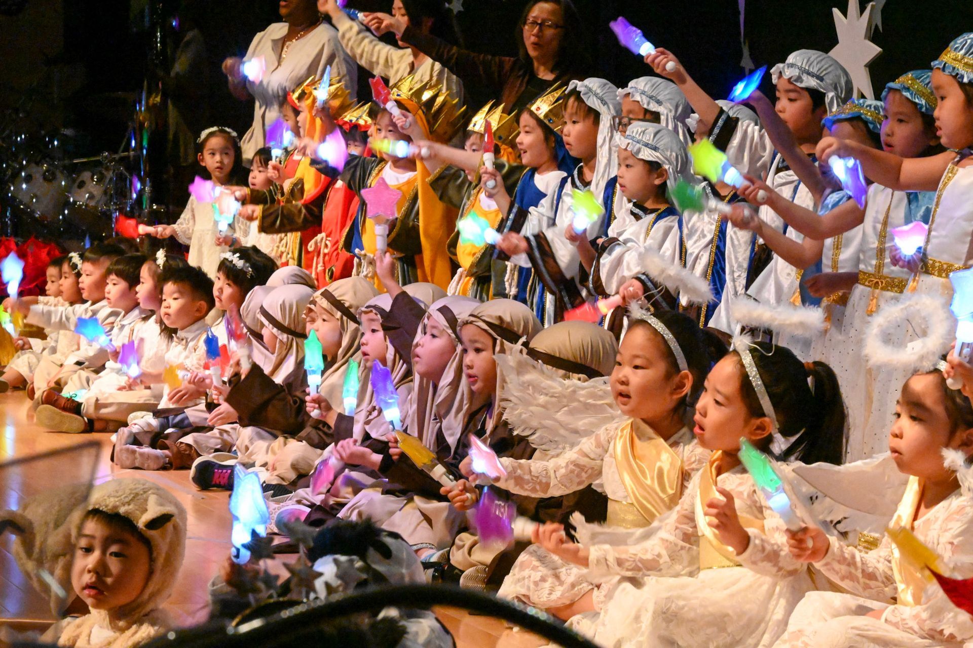 Children in costumes perform a Christmas play, holding glowing wands.