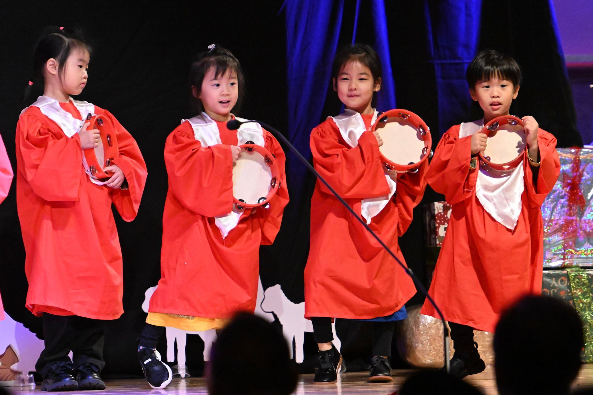 Four children in red robes with tamborines on stage.