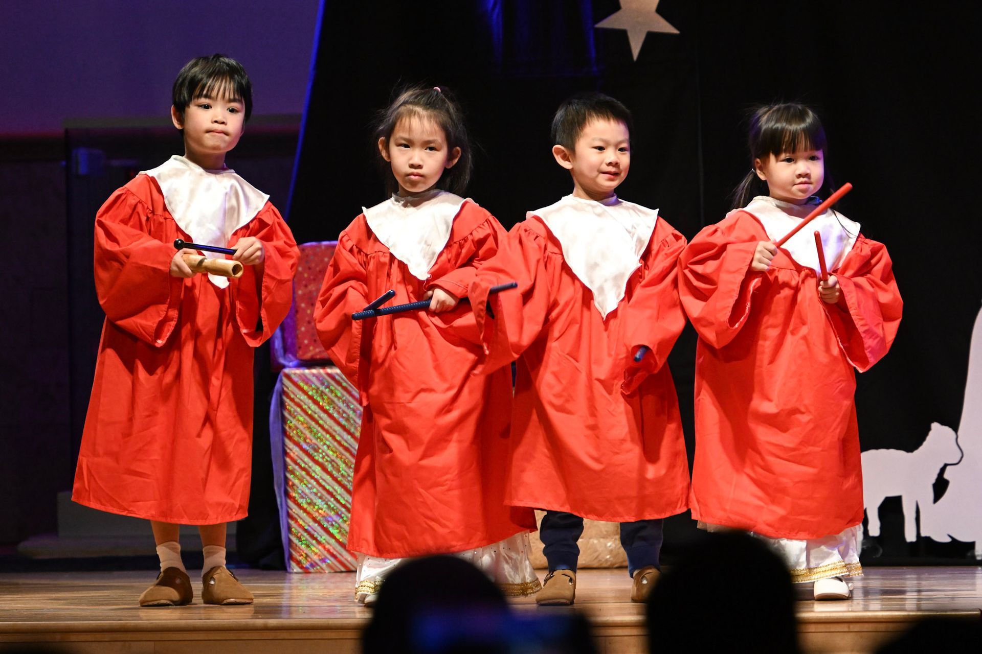 Children in red robes performing on a stage, holding instruments.