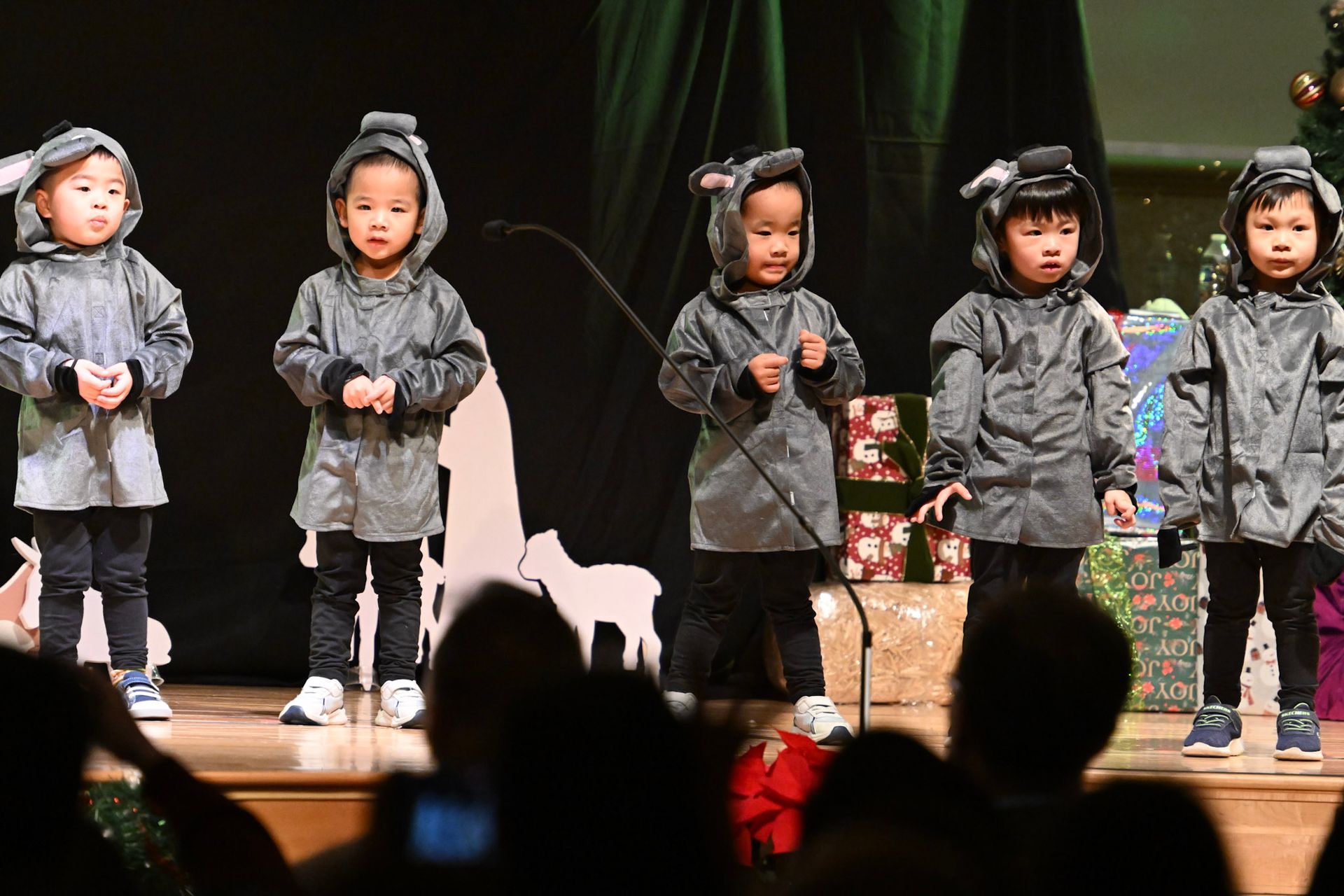 Children in gray mouse costumes on stage, performing. Decorated backdrop, audience in foreground.