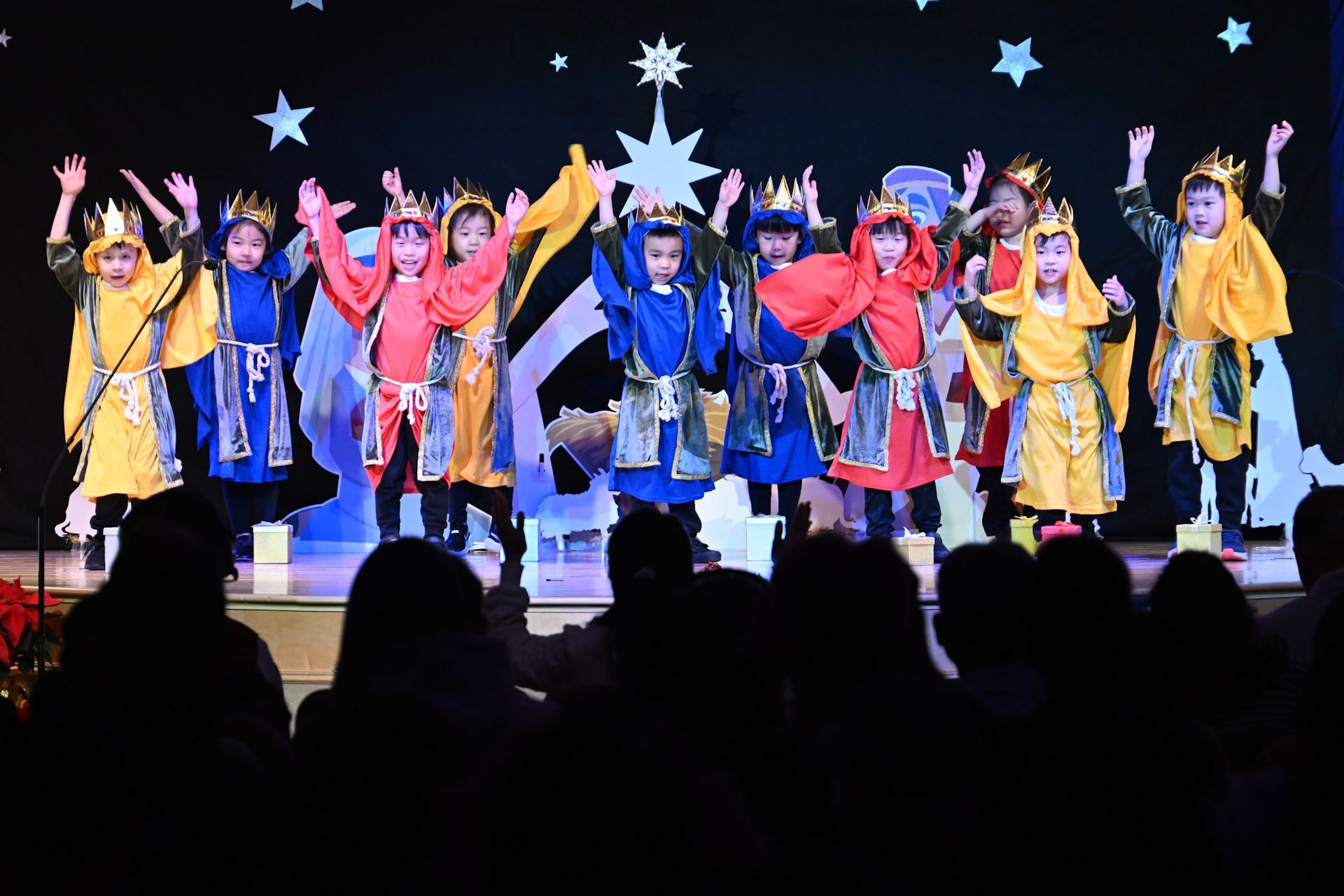 Children in colorful costumes performing on stage with an audience.