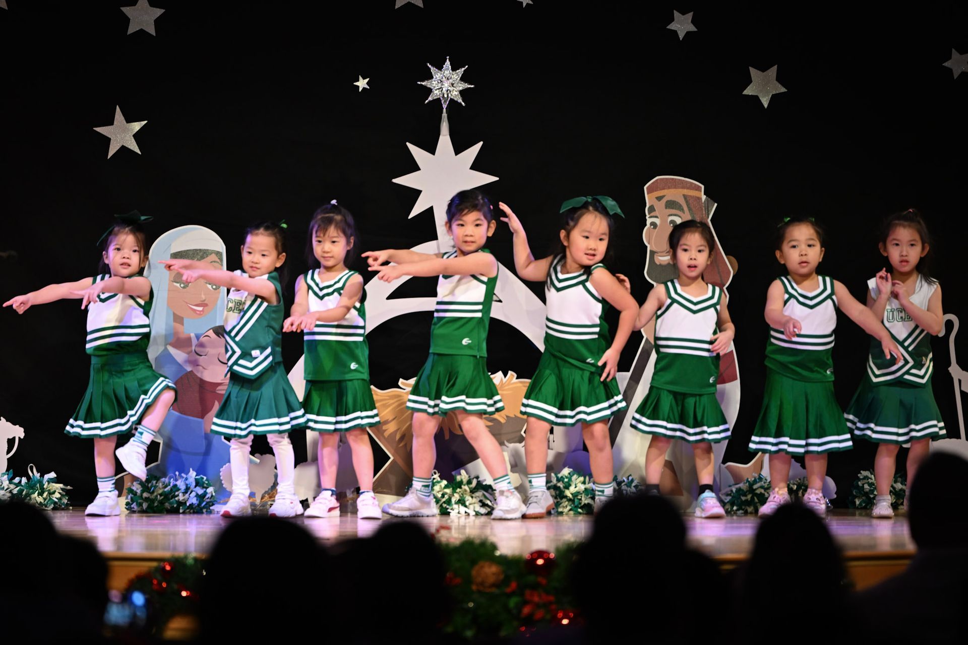 Children in green and white cheerleader outfits performing on stage.